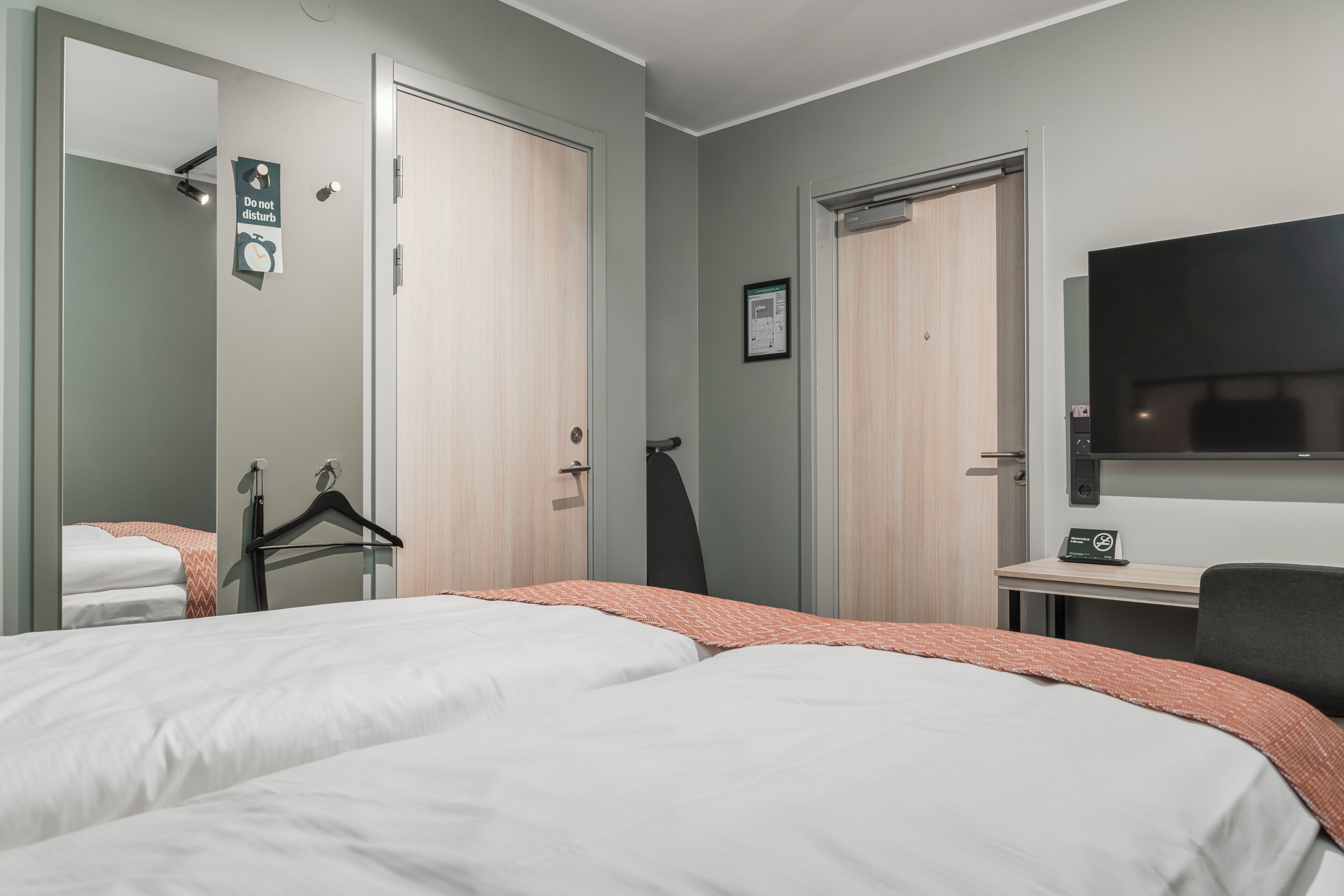 A hotel room with two beds, a desk, a TV, and a mirror.