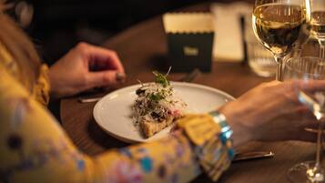 A person dining at a table with a plate of food and a glass of wine.