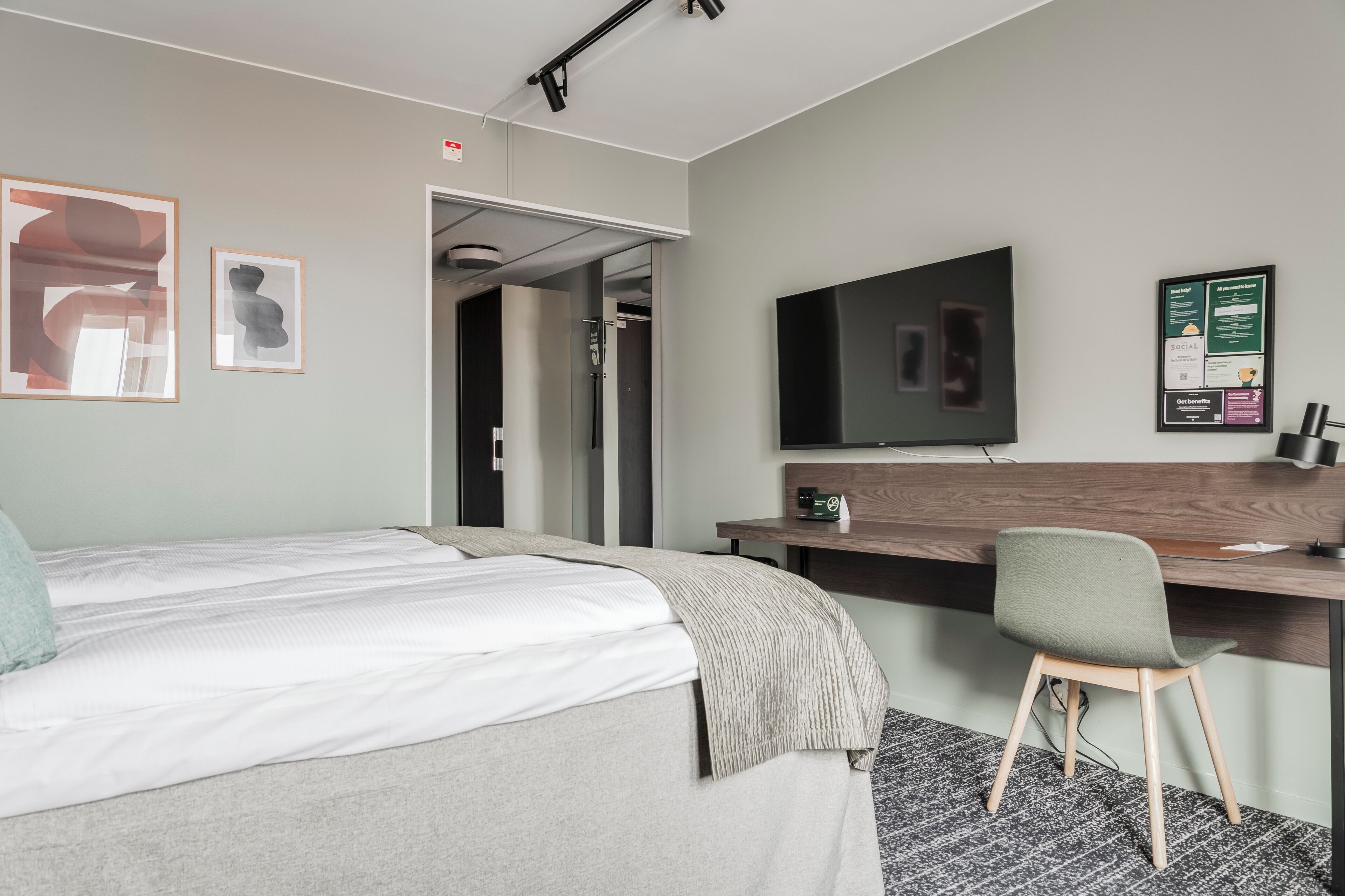 Une chambre d’hôtel avec un lit, un bureau, une chaise, une télévision et une affiche au mur.