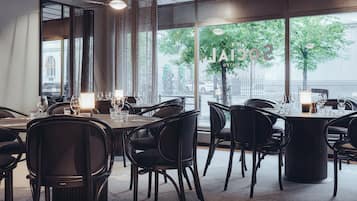 A restaurant with a view of the river, featuring round tables and black chairs.