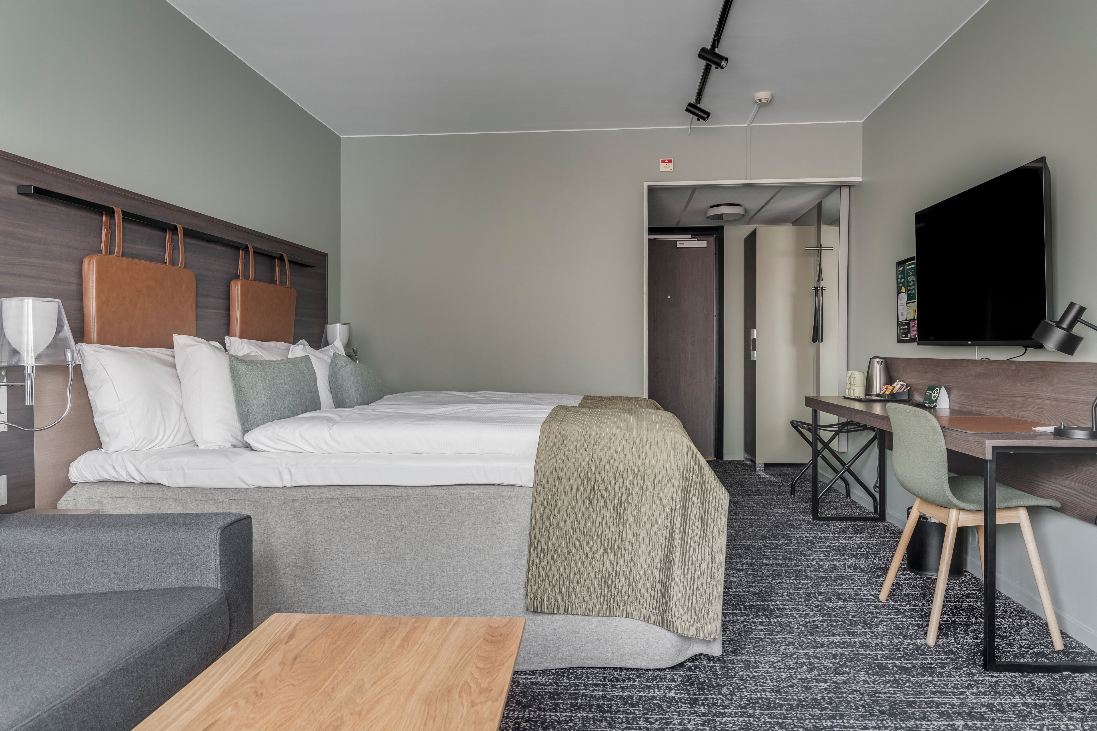 A hotel room with a bed, a desk, a chair, a television, and a coffee table.