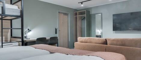 A modern hotel room with a bunk bed, a desk with a chair, a sofa, and a wardrobe.