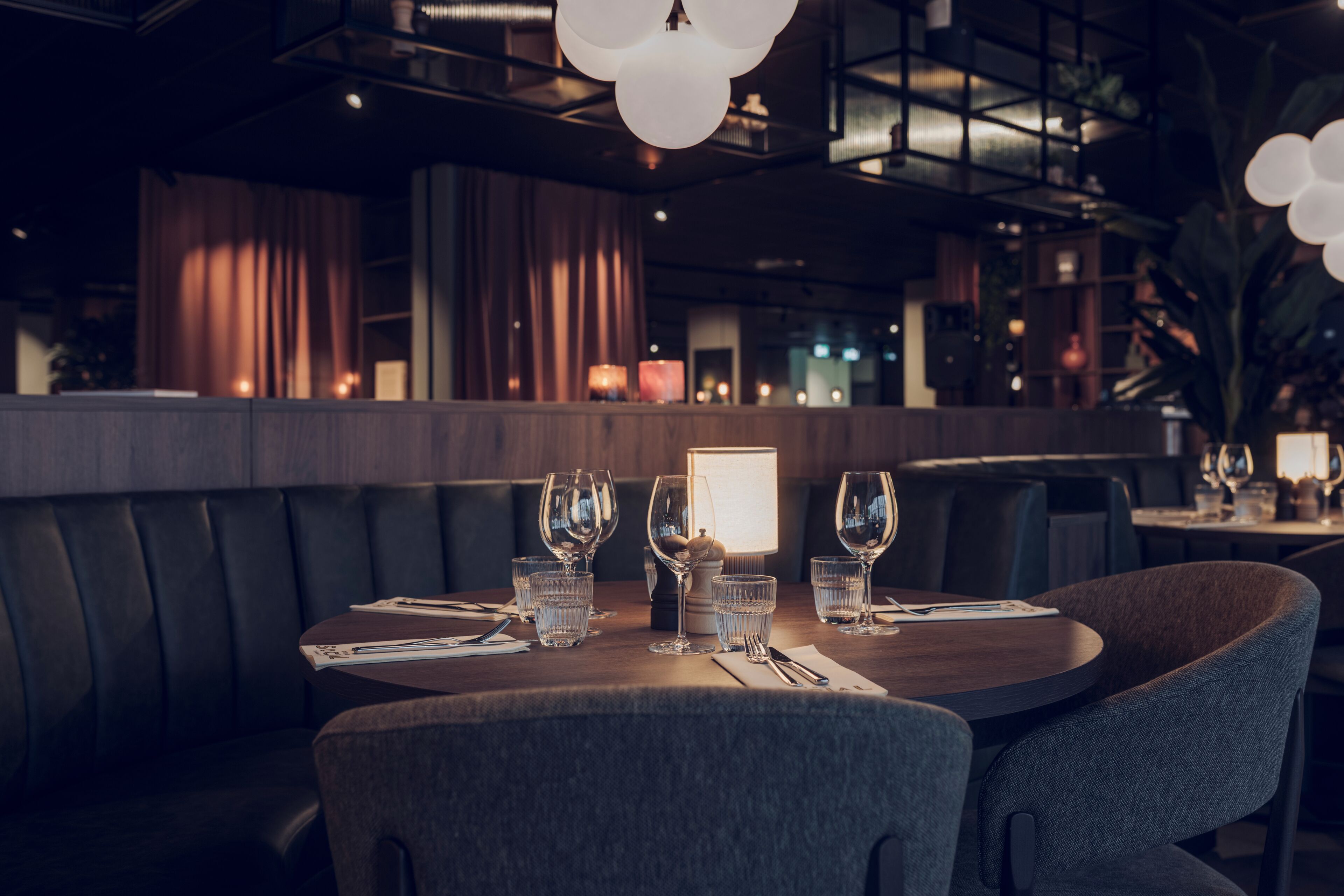 A restaurant with a dark interior, leather booth seating, and a table set with wine glasses and water glasses.