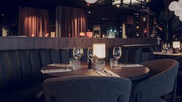 A restaurant with a dark interior, leather booth seating, and a table set with wine glasses and water glasses.