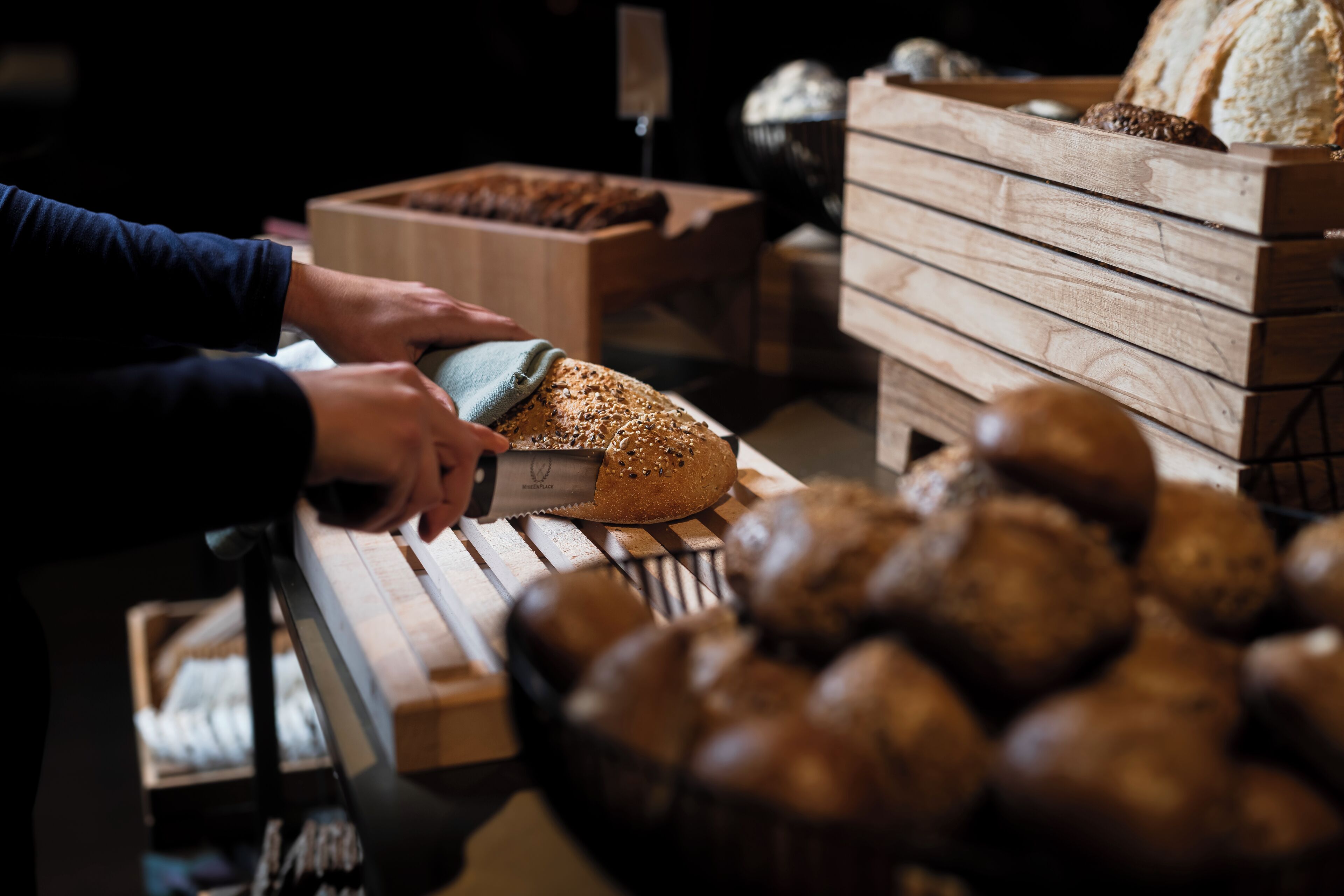 A person slicing bread from a wooden bread box.