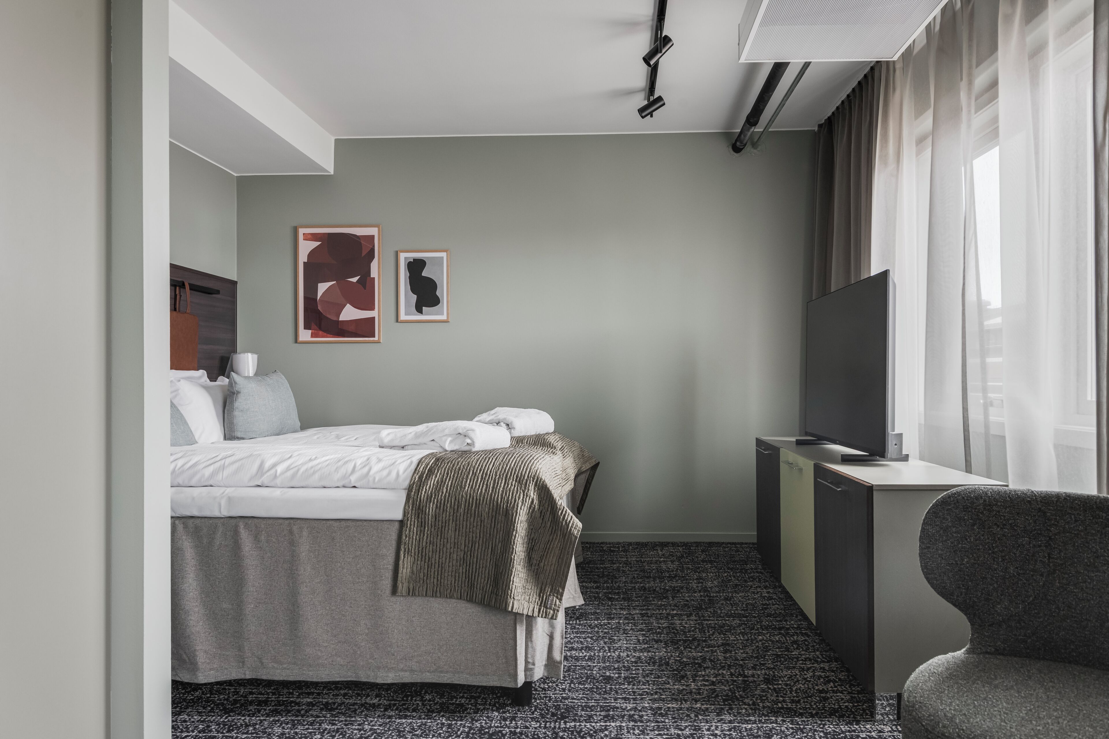Ein Hotelzimmer mit Bett, Schreibtisch, Sessel, Fernseher und Bildern an der Wand.