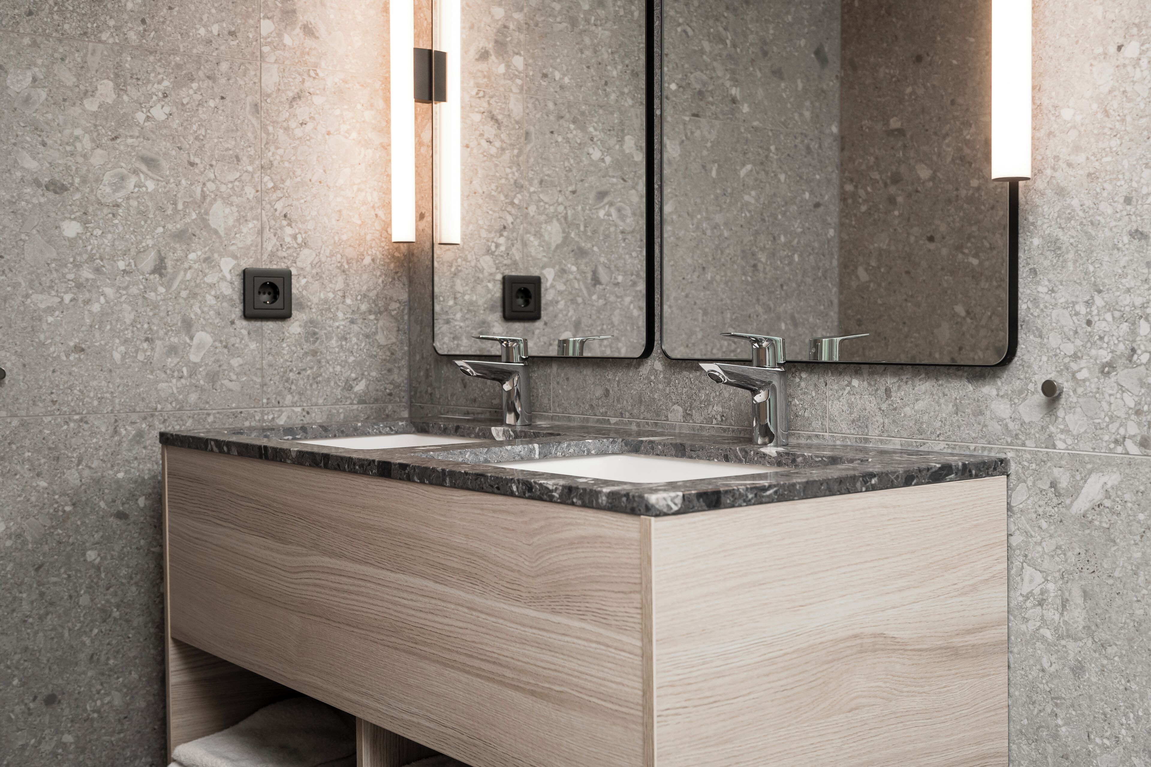 A modern bathroom with two sinks, wooden vanity, and granite countertops.