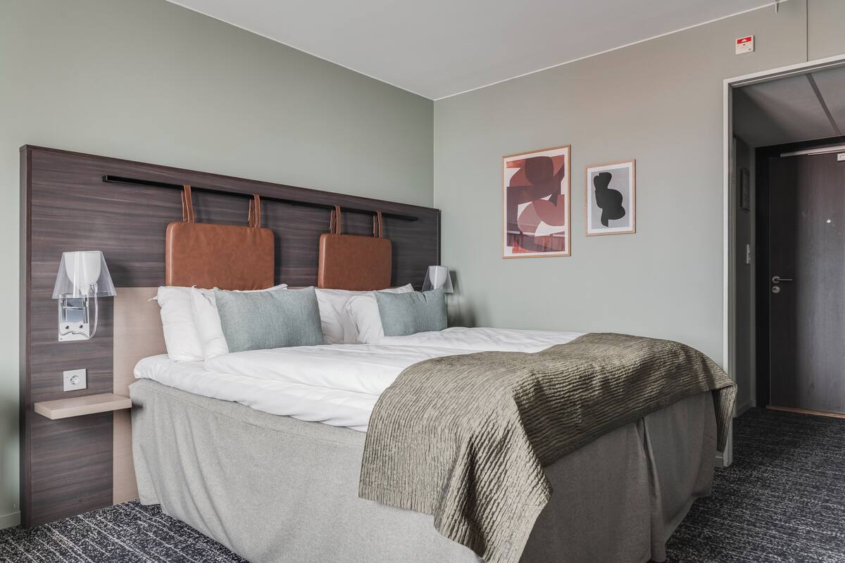 Habitación de hotel con cama, mesita de noche, lámpara y una obra de arte en la pared.