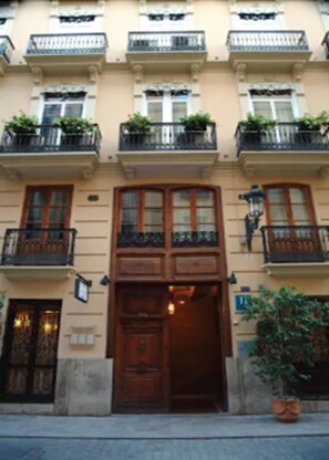 Un edificio con puerta de madera central, varias ventanas y balcones con plantas.
