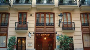 Un edifici amb entrada central, plantes en testos a banda i banda, i balcons amb baranes.