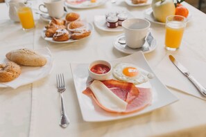 Un desayuno con cruasanes, huevos, jamón y jugo de naranja sobre una mesa.