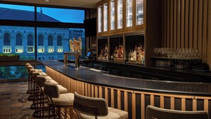 A bar area with a long counter, multiple bar stools, and a view of a building through large windows. - The Westin Copley Place, Boston, a Marriott Hotel (Boston)