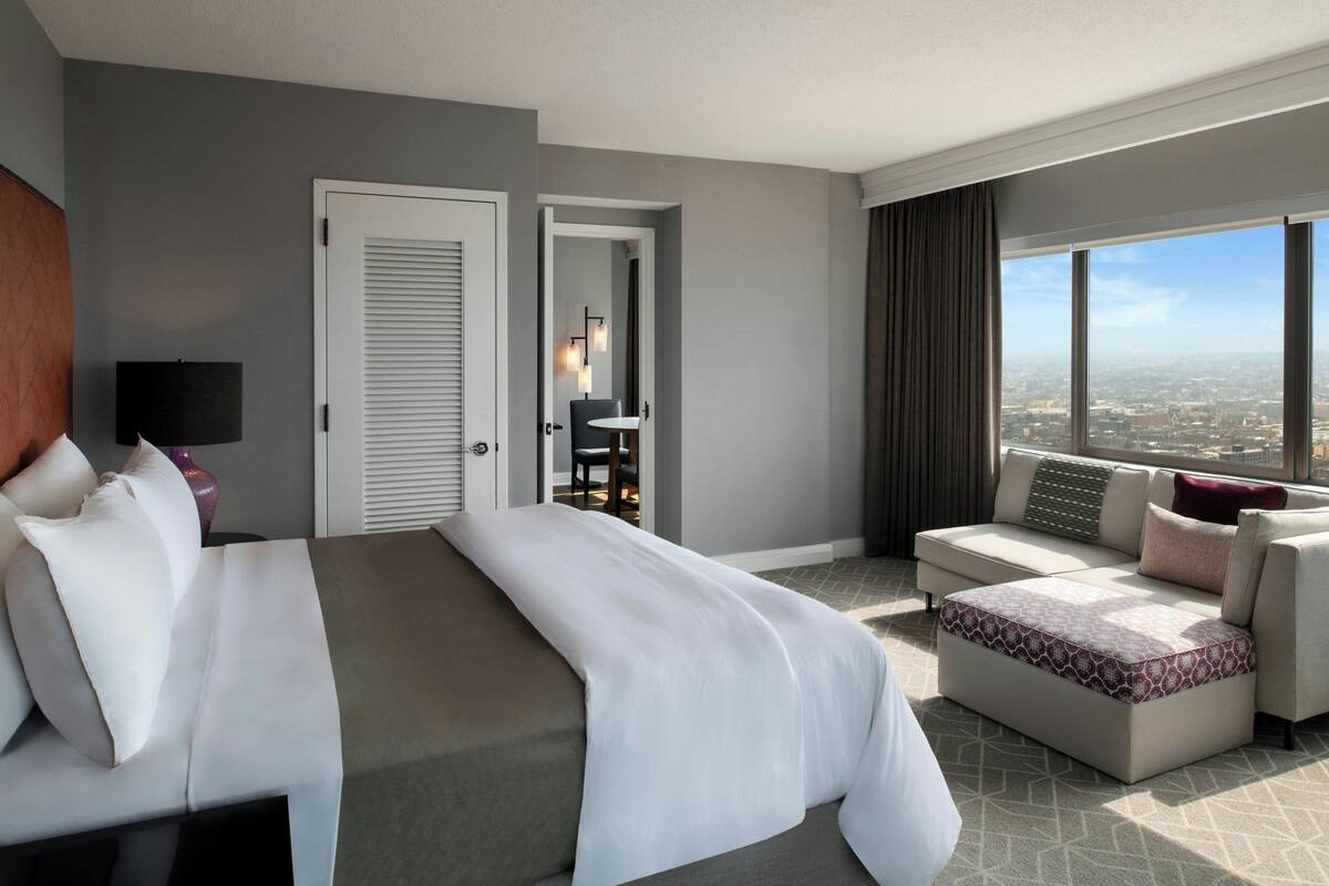 Habitación de hotel moderna con una cama grande, un sofá, una mesita y vistas a la ciudad.