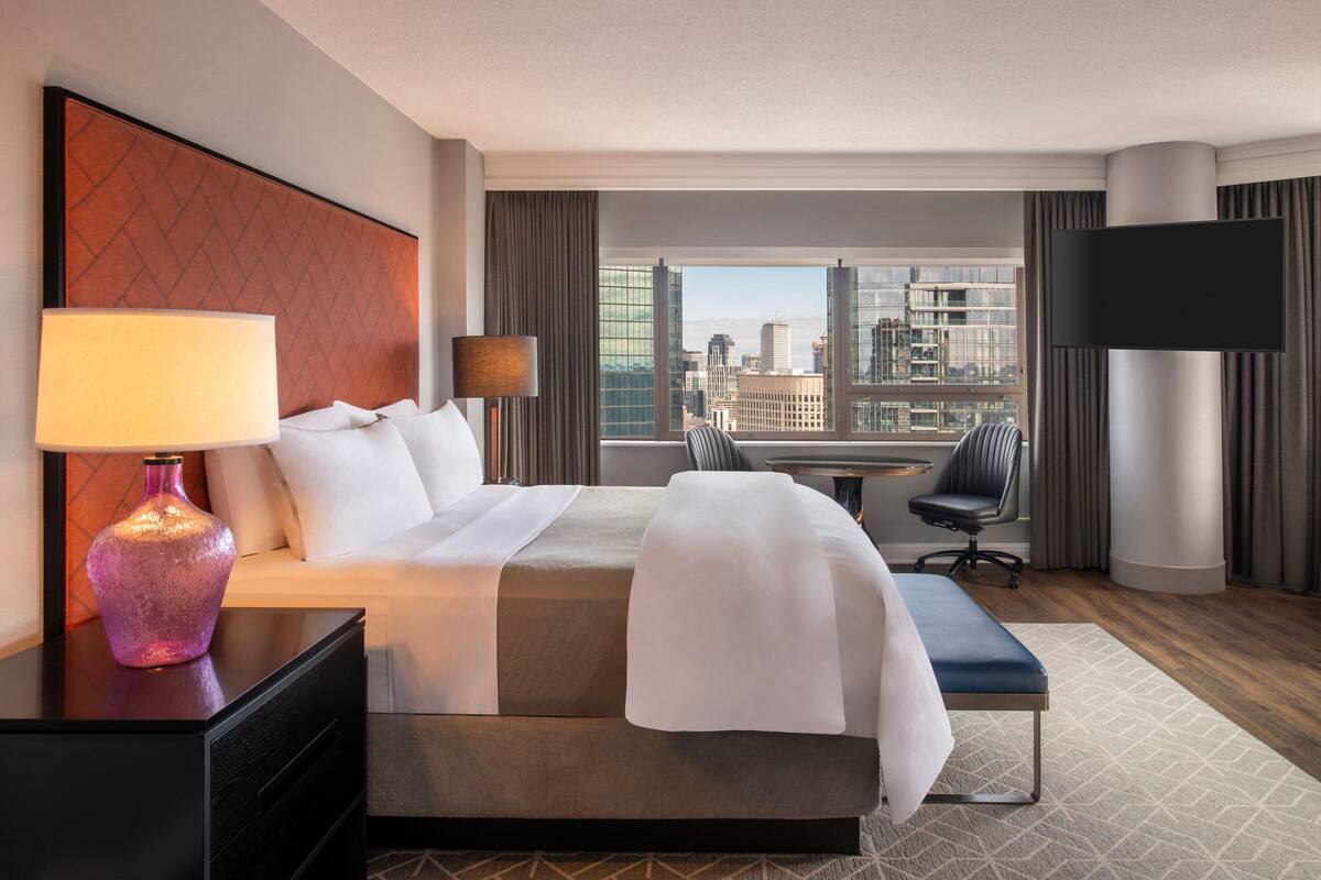 Una habitación de hotel con una cama grande, un escritorio con lámpara, una silla y un televisor.