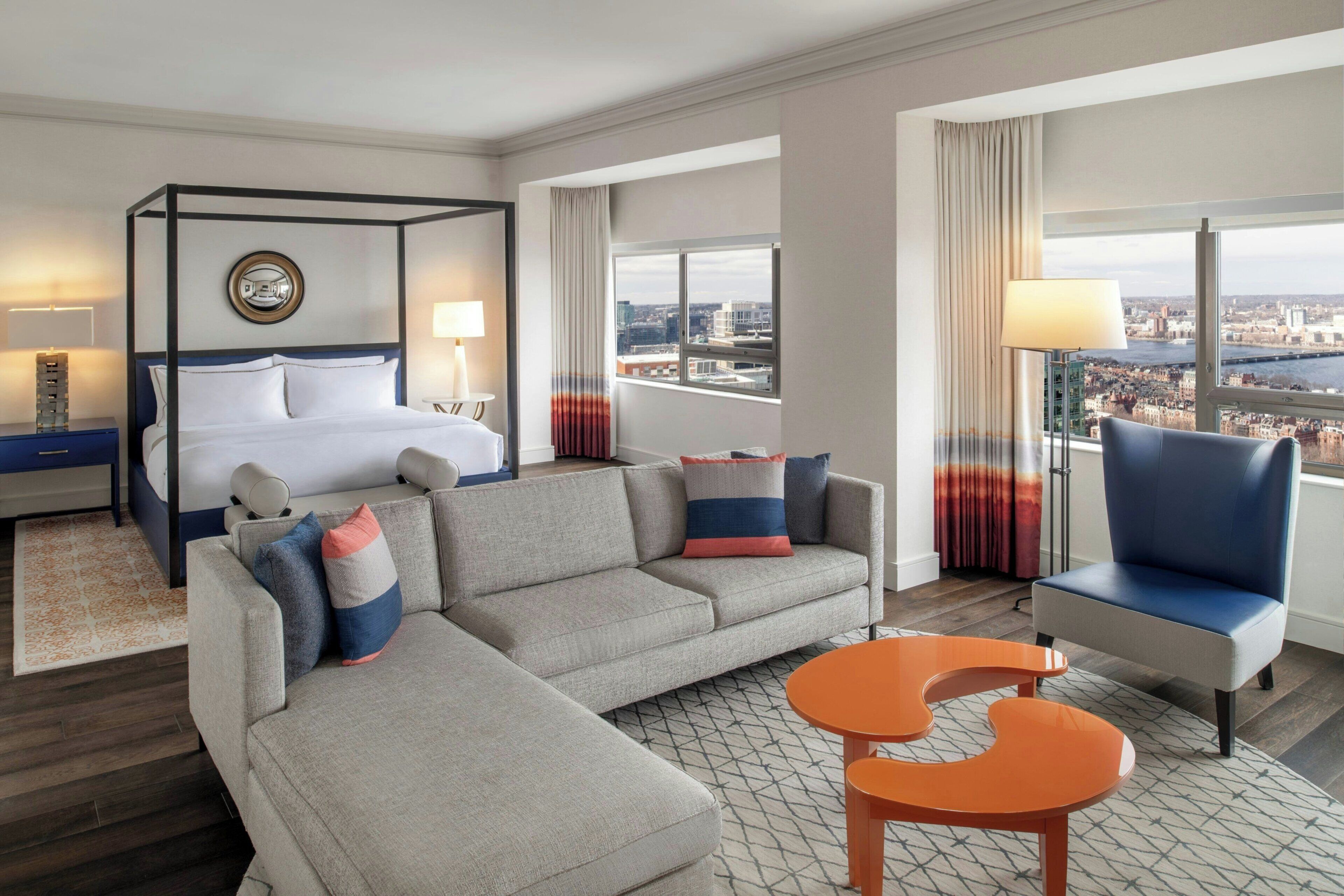 A modern hotel room with a four-poster bed, a sofa, a chair, and a small table.