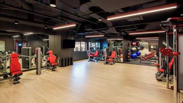 A gym with various exercise machines, mirrors, and a wooden floor.