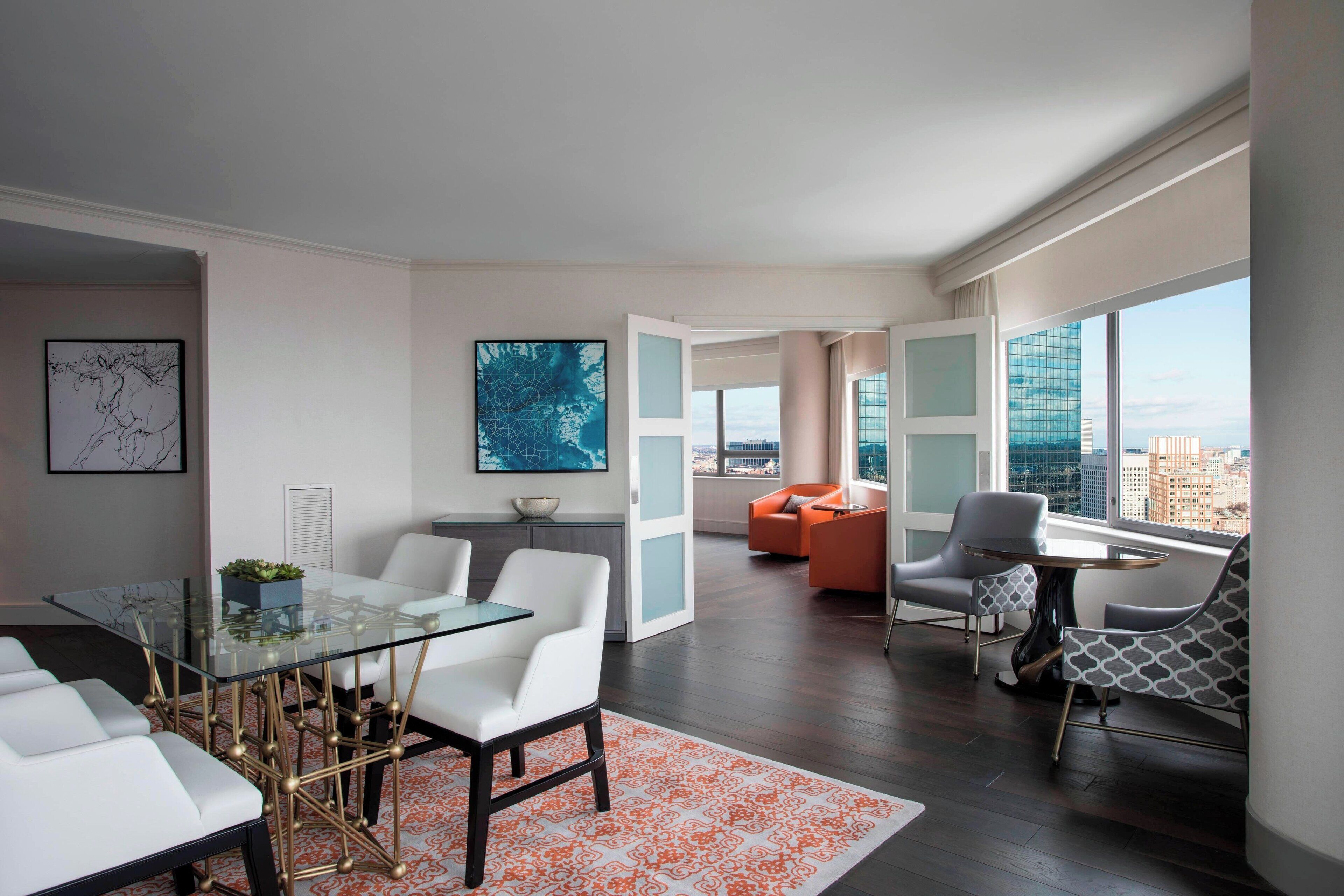 Una sala moderna con una mesa de comedor de vidrio, sofás blancos y sillones de color naranja.
