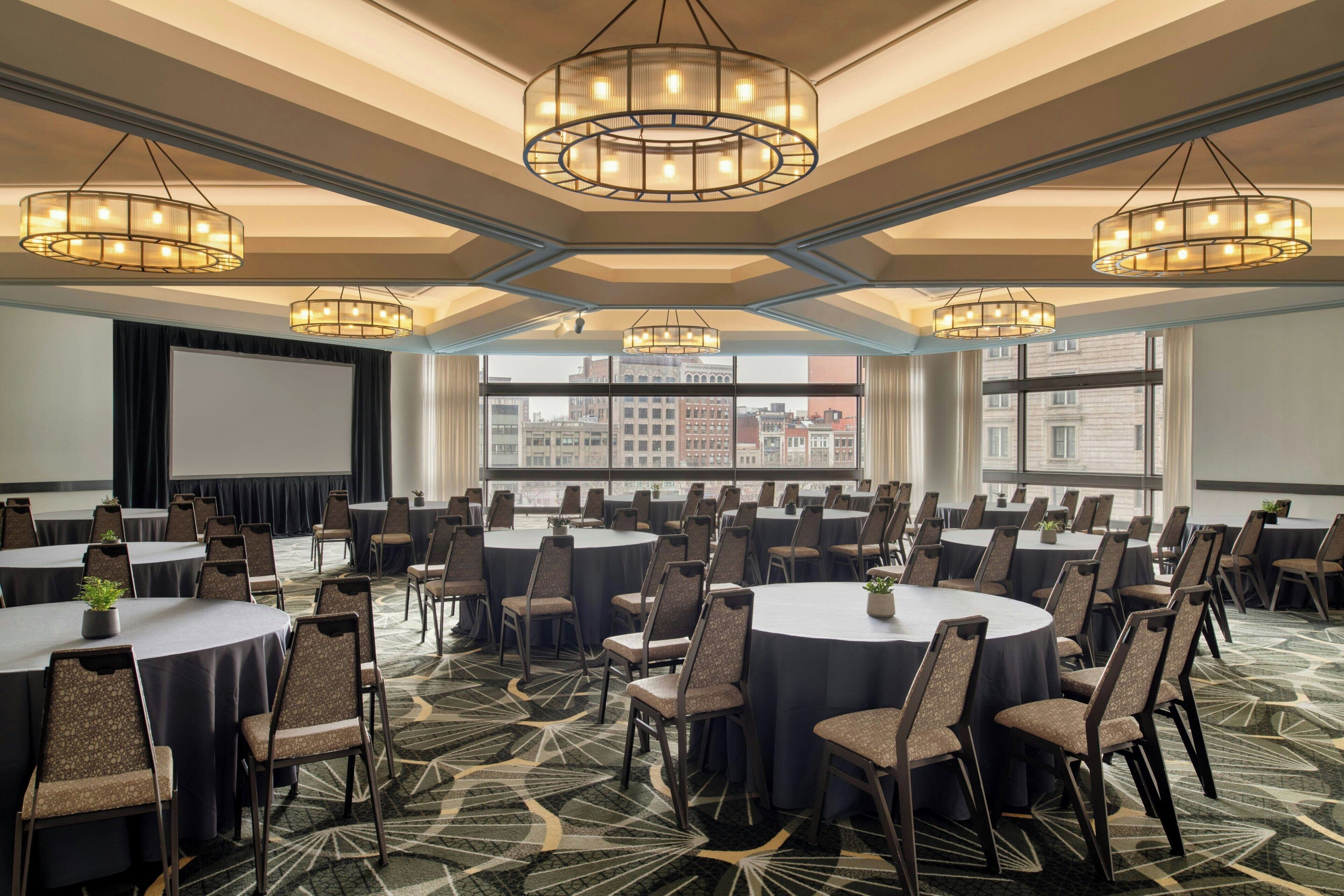 A conference room with round tables, chairs, and a large screen.