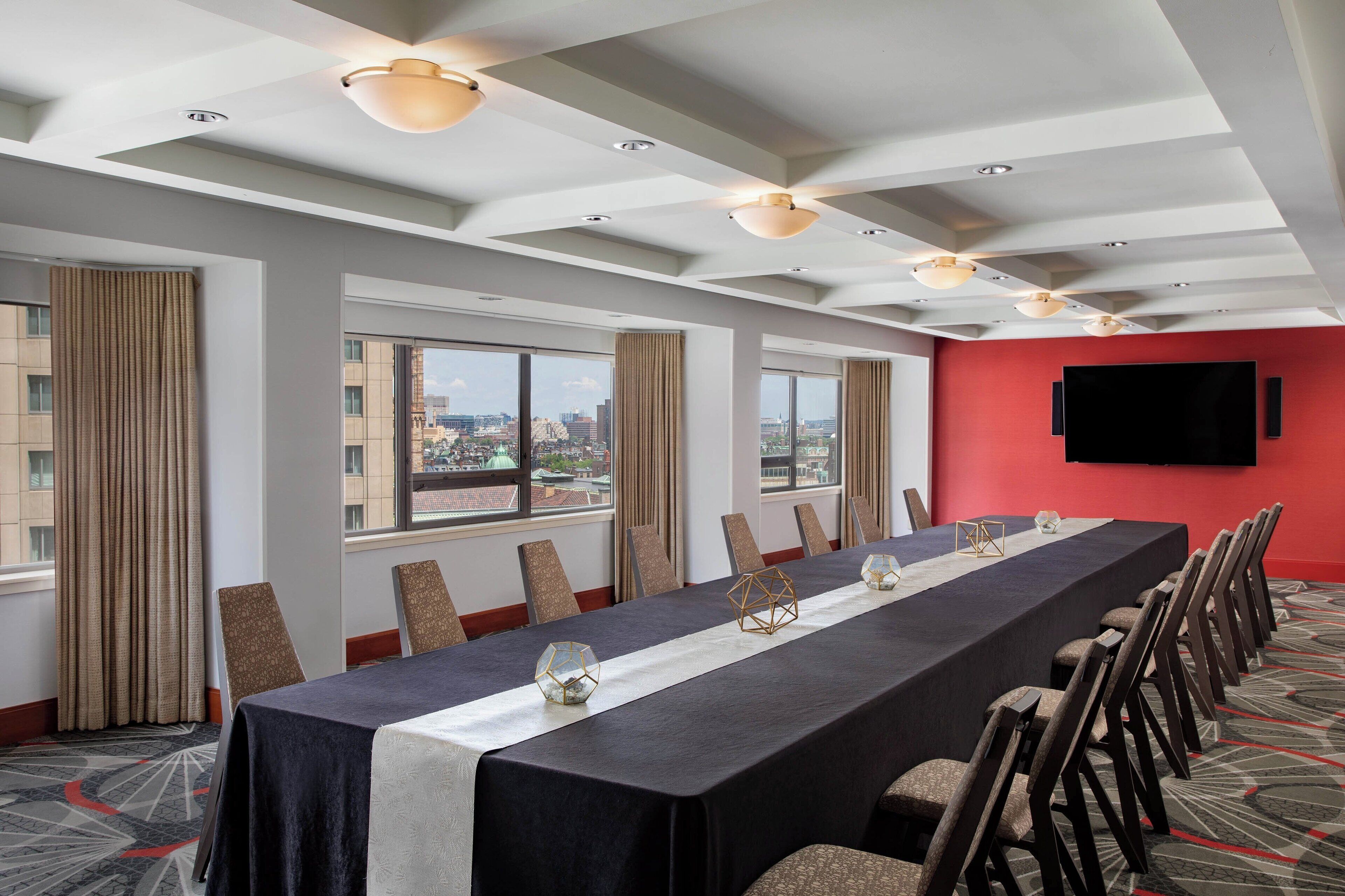 A conference room with a long table, chairs, a flat-screen TV, and large windows with curtains.