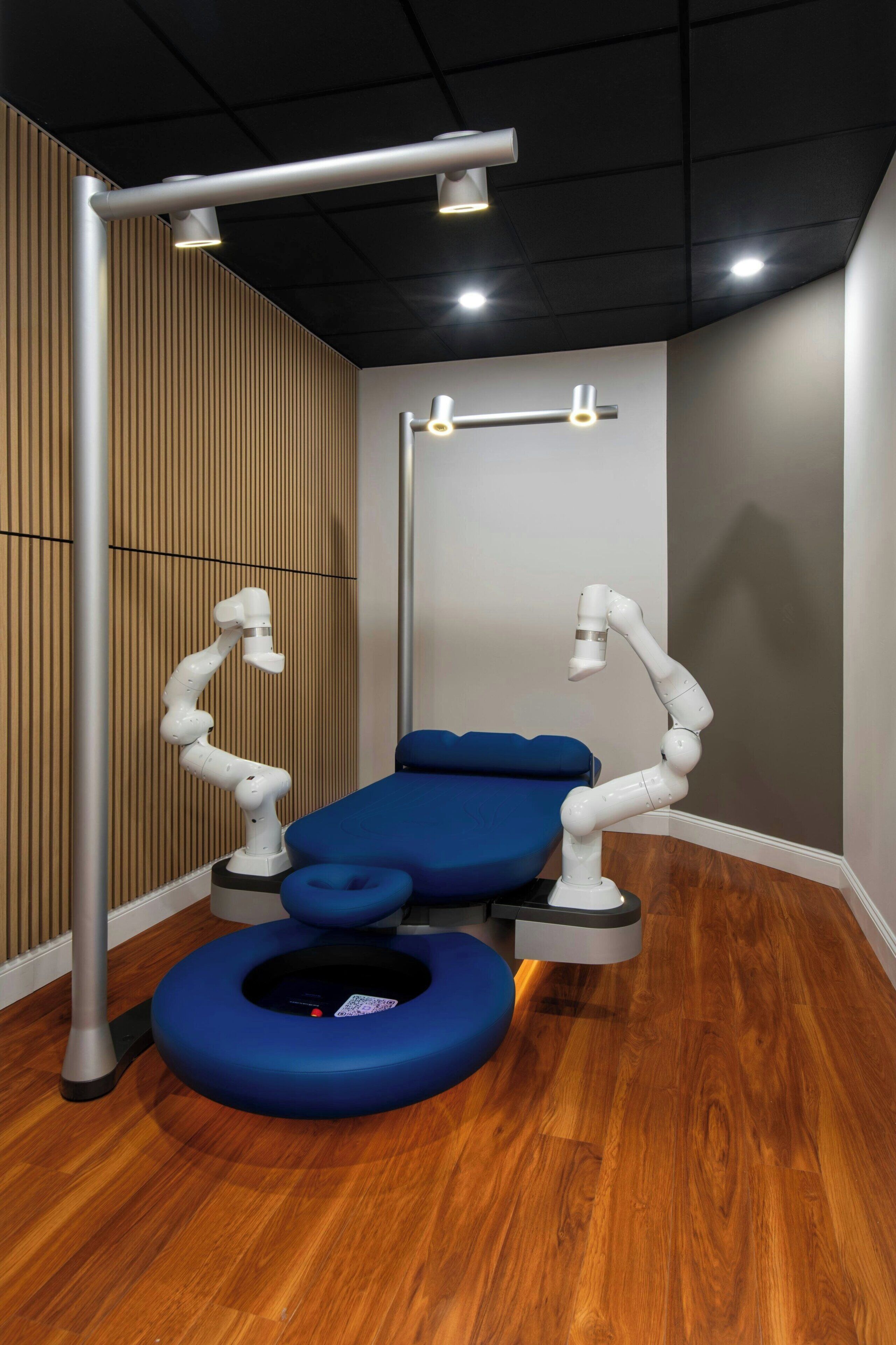 A modern dental clinic with a blue examination chair, overhead lighting, and a wooden wall panel.