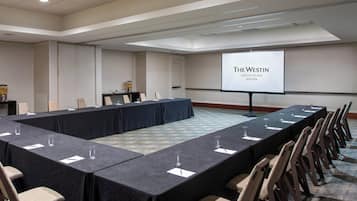 A conference room with a long table, chairs, a projector screen displaying "The Westin Copley Place Boston", and a small table with a coffee machine.