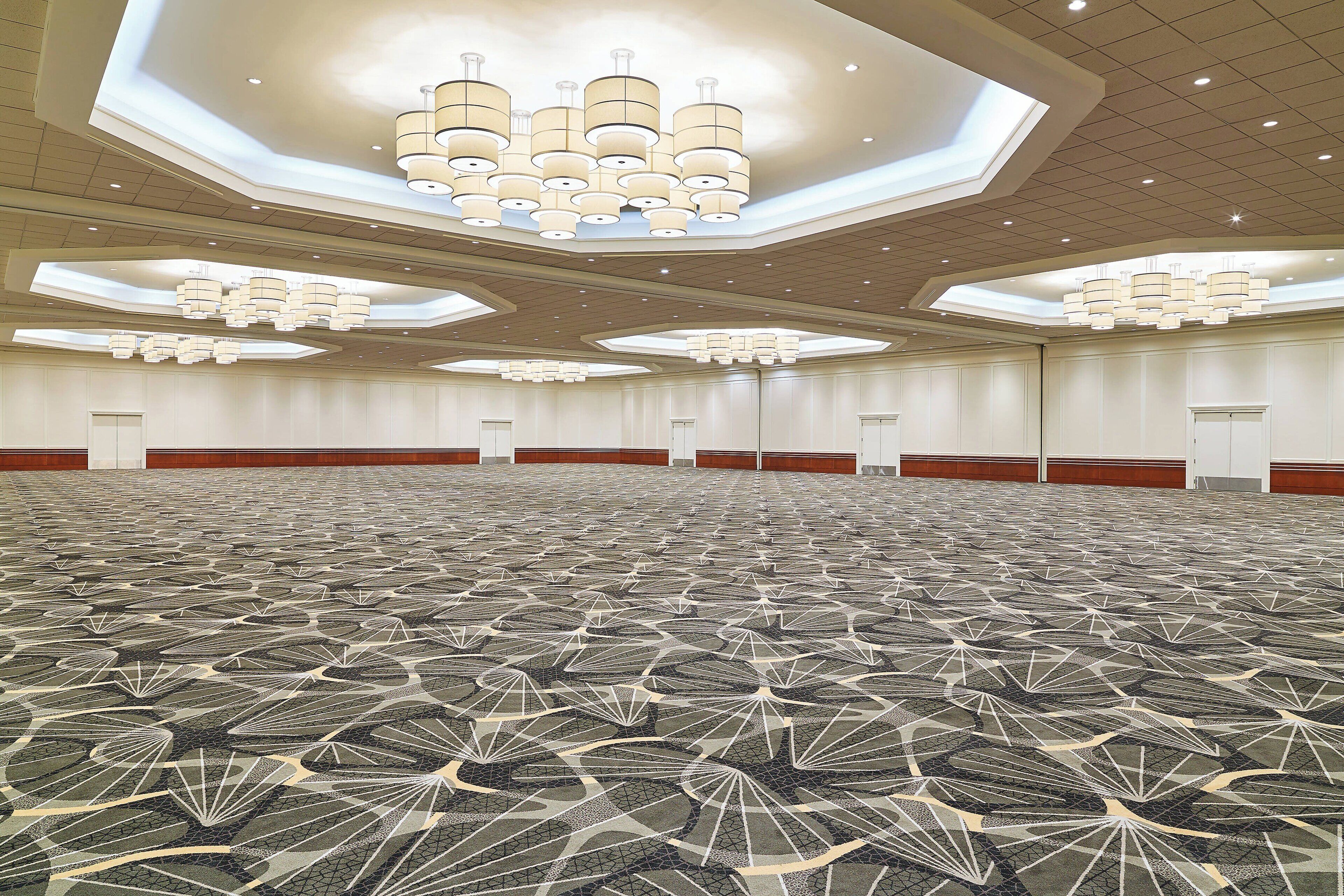 A large conference room with a patterned carpet, multiple chandeliers, and a high ceiling.