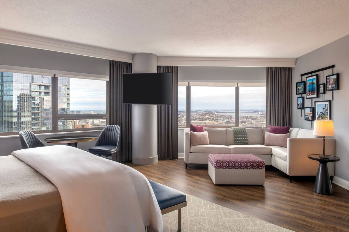 Habitación de hotel moderna con una cama grande, un sofá, una silla, un televisor y vista a la ciudad.