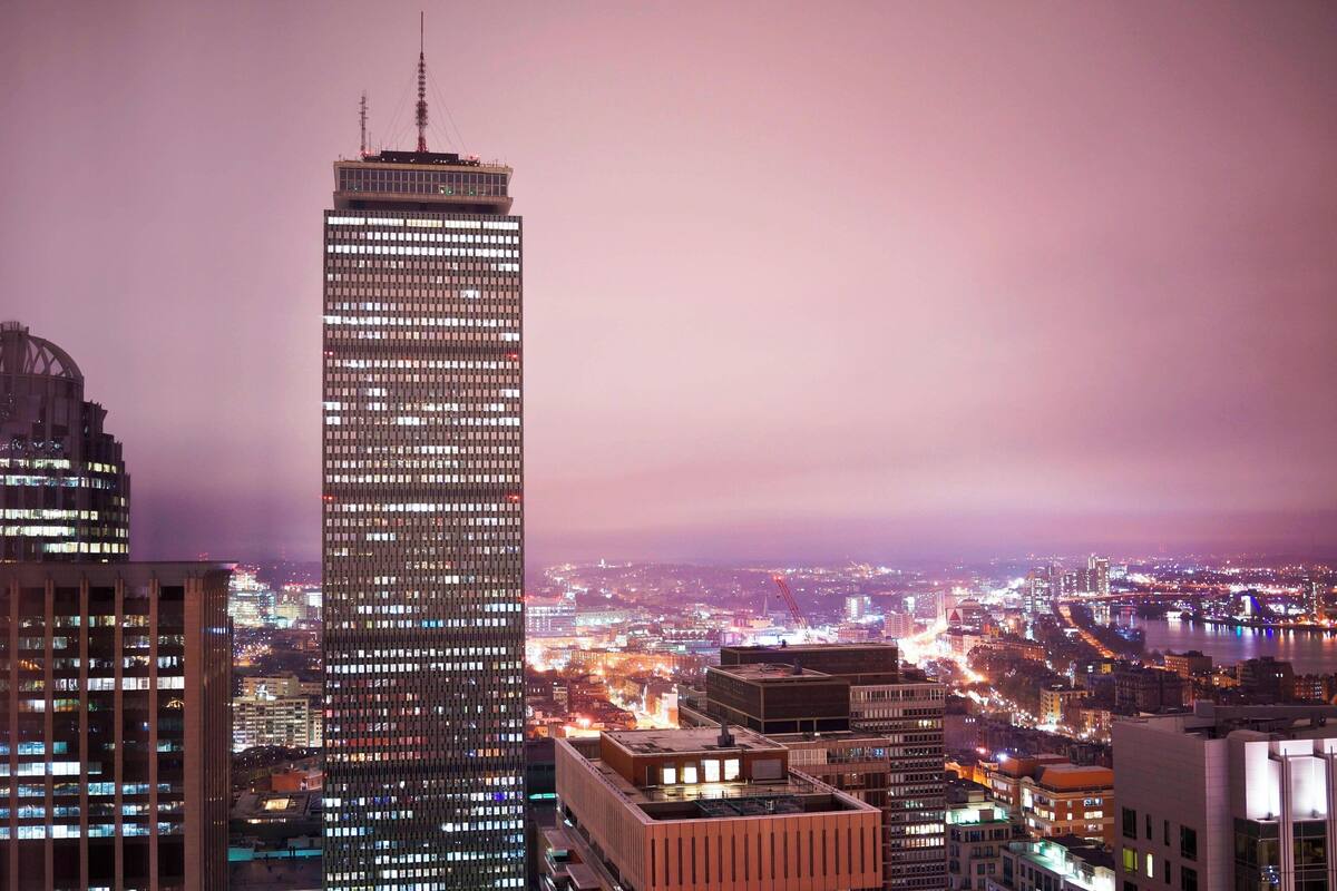Un edificio de gran altura con un diseño arquitectónico moderno, rodeado de otros edificios y un río al fondo.