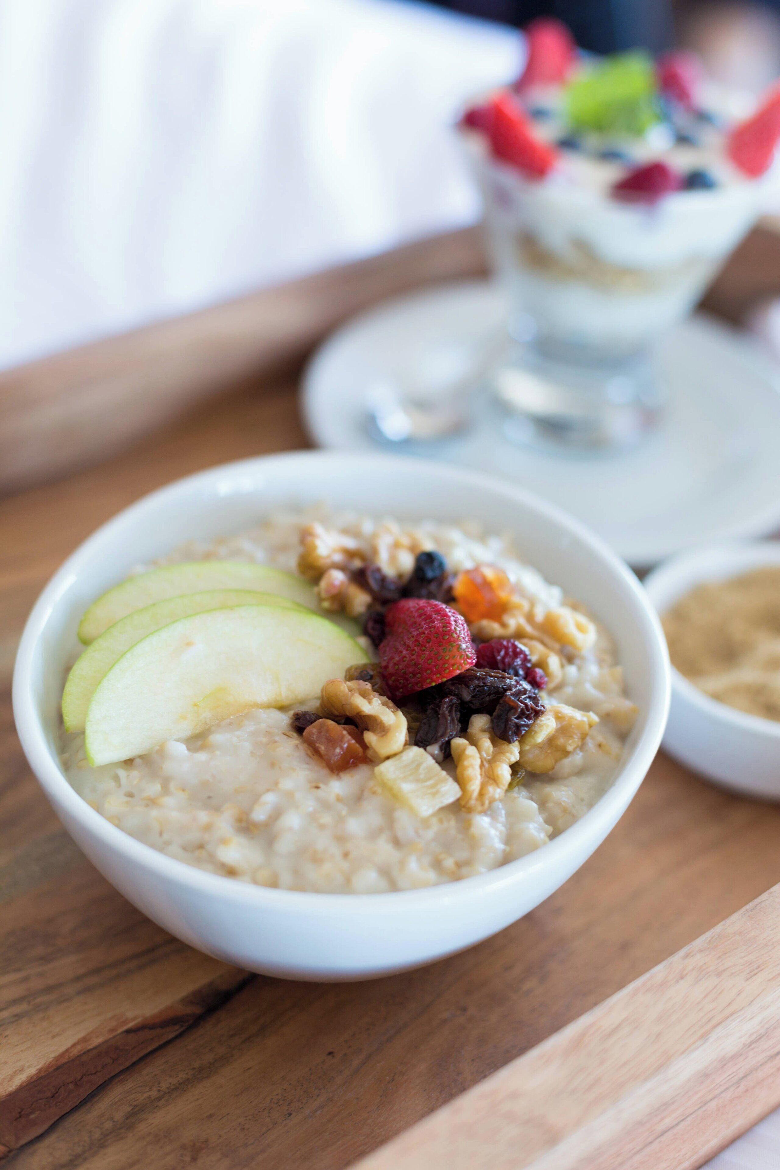 A bowl of oatmeal topped with sliced apples, strawberries, and nuts.