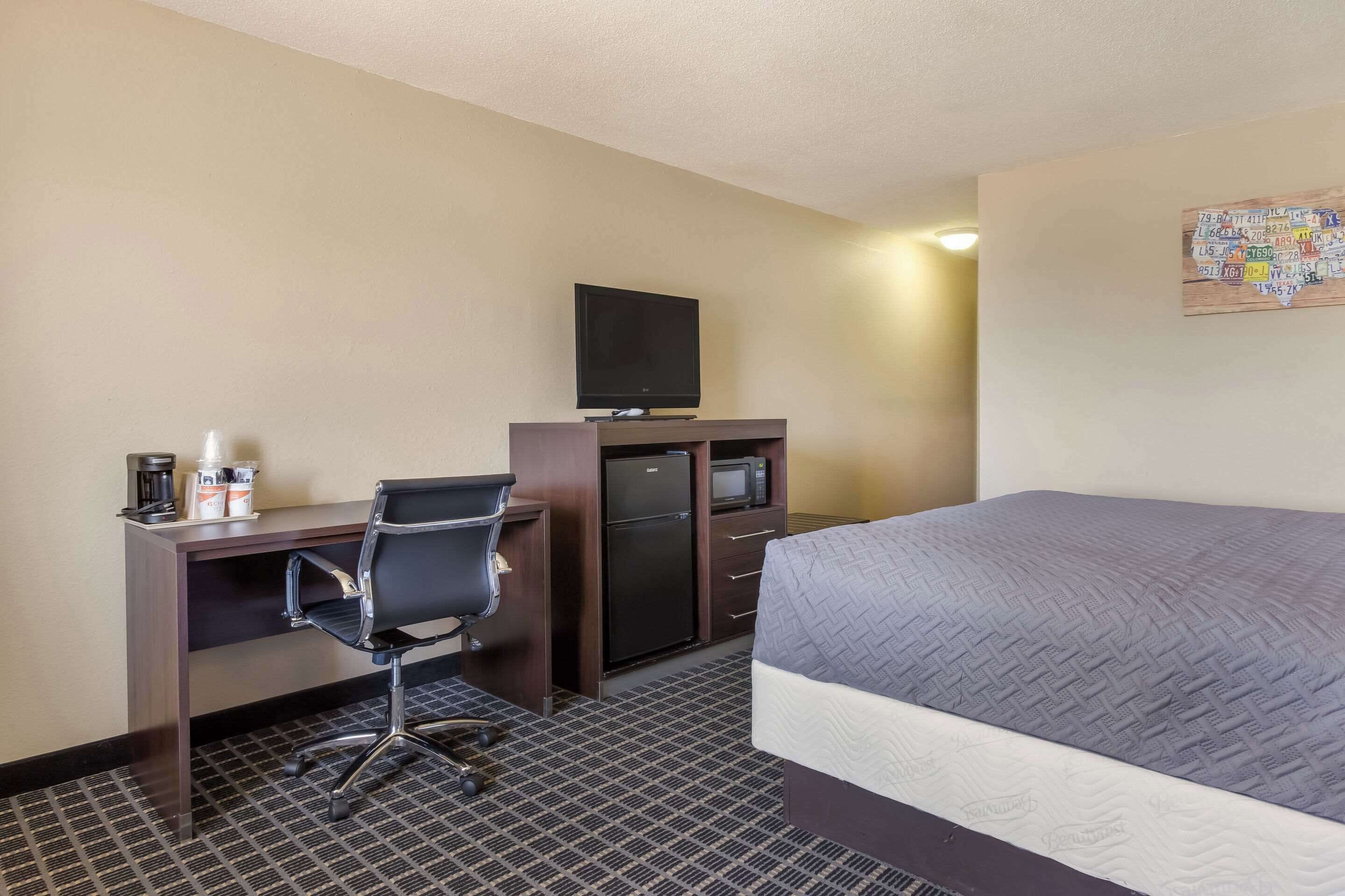 Habitación de hotel con una cama, un escritorio con computadora, televisor y microondas.