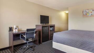 Habitación de hotel con una cama, un escritorio con computadora, televisor y microondas.