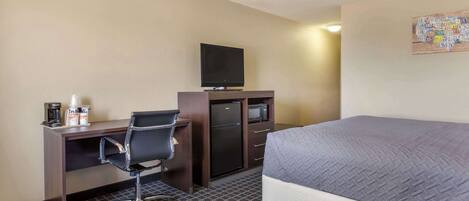 Une chambre d’hôtel équipée d’un lit, d’un bureau avec un ordinateur, d’une télévision et d’un four à micro-ondes.