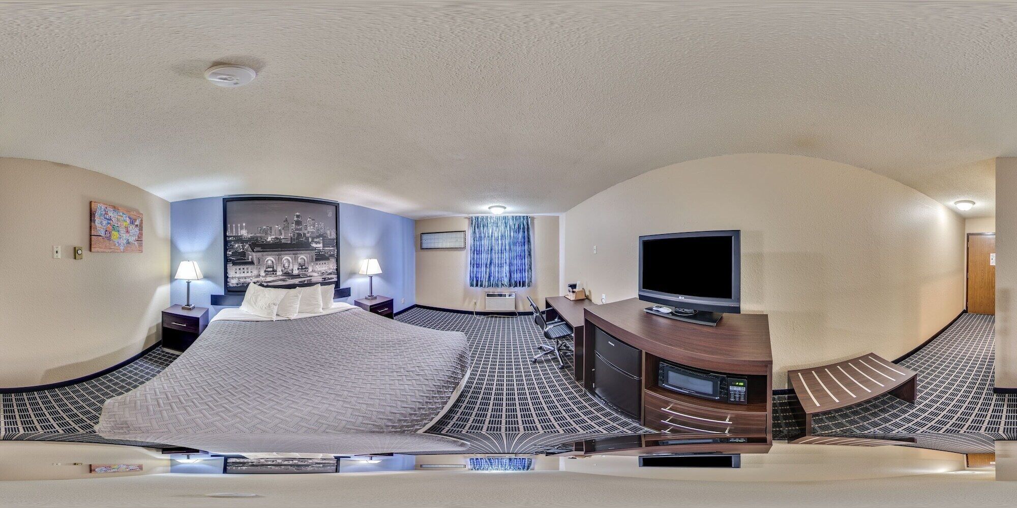 A hotel room with a bed, a desk, a TV, and a view of a cityscape.