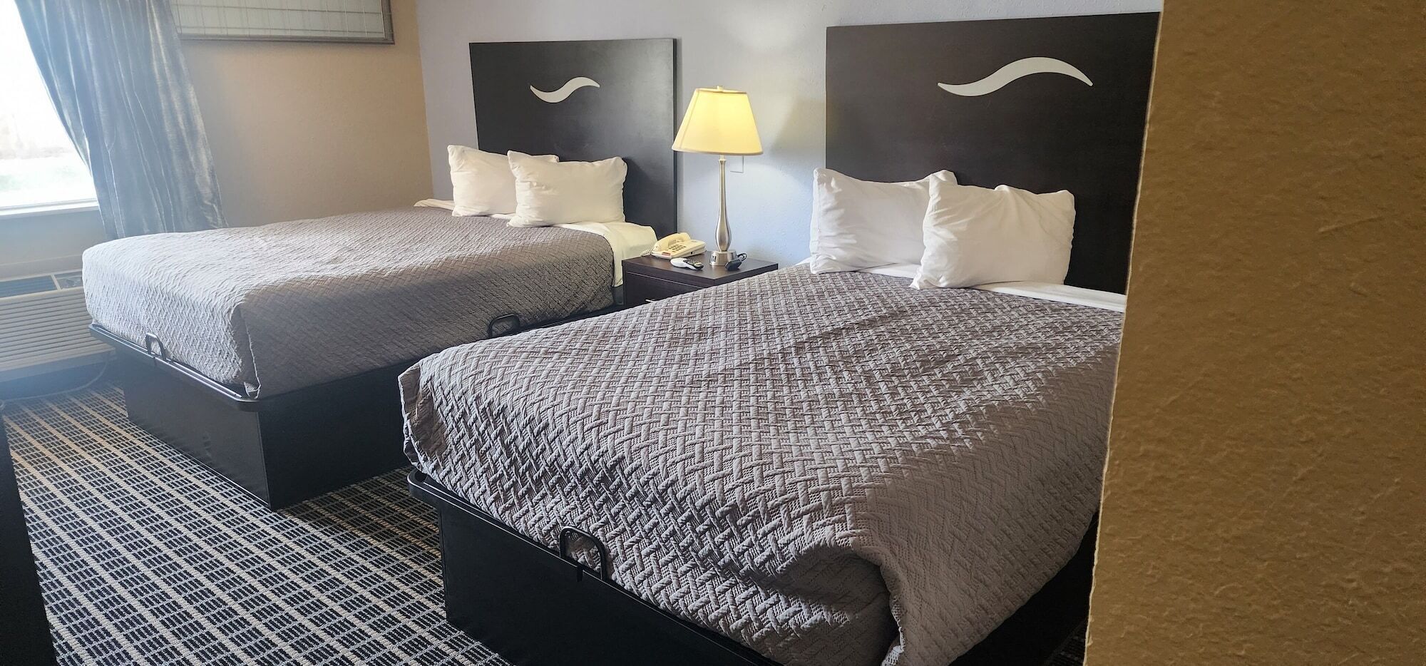 Een hotelkamer met twee bedden, een nachtkastje met een lamp en een telefoon.