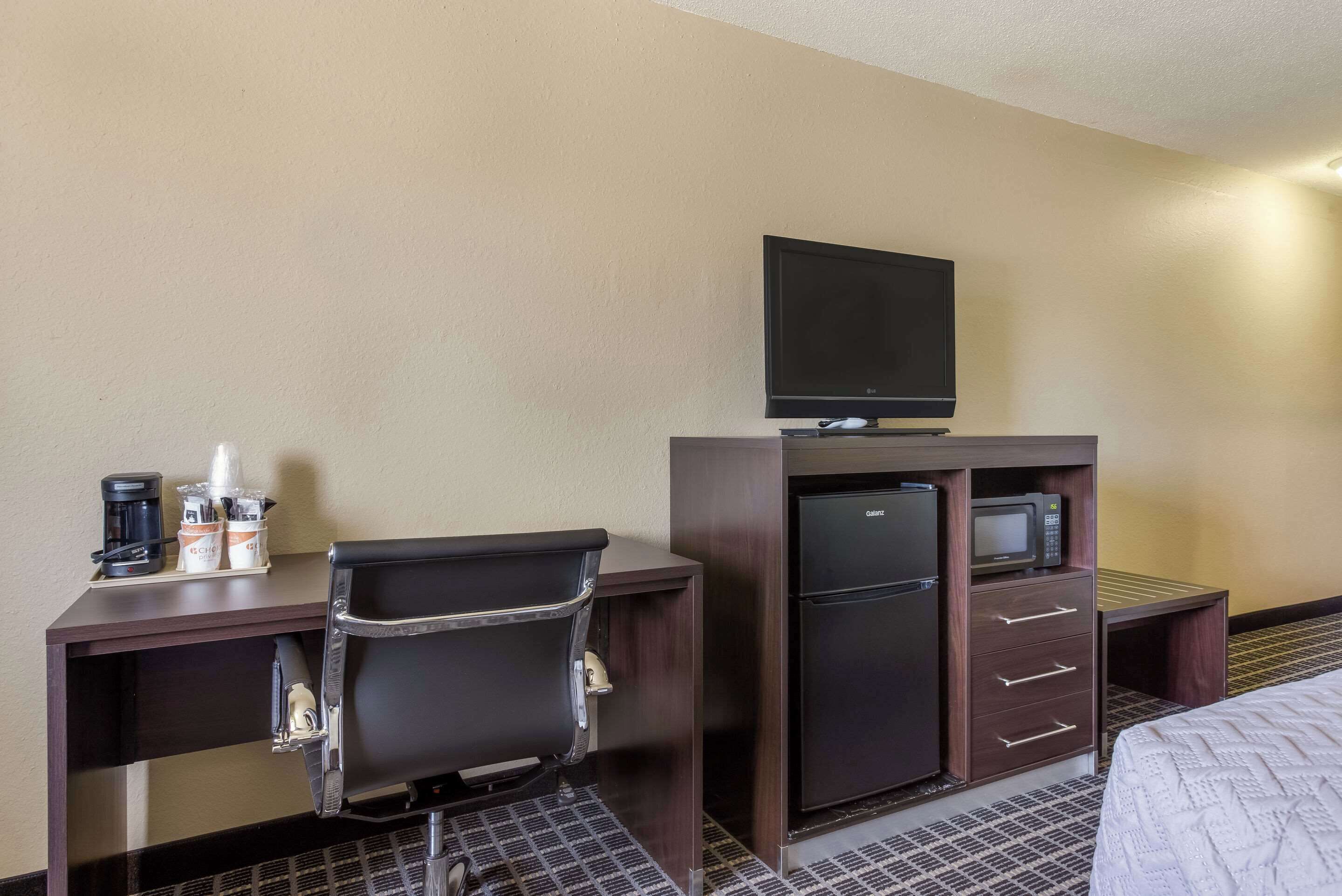 Ein Hotelzimmer mit Schreibtisch, Stuhl, Fernseher, Minibar und einem Bett.