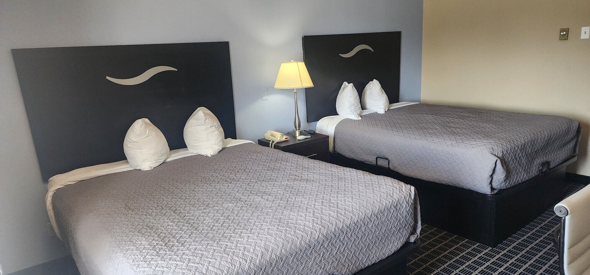 A hotel room with two beds, each with a headboard, a bedside table with a lamp, and a telephone.