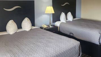 A hotel room with two beds, each with a pillow and a headboard. There is a nightstand with a lamp and a phone.