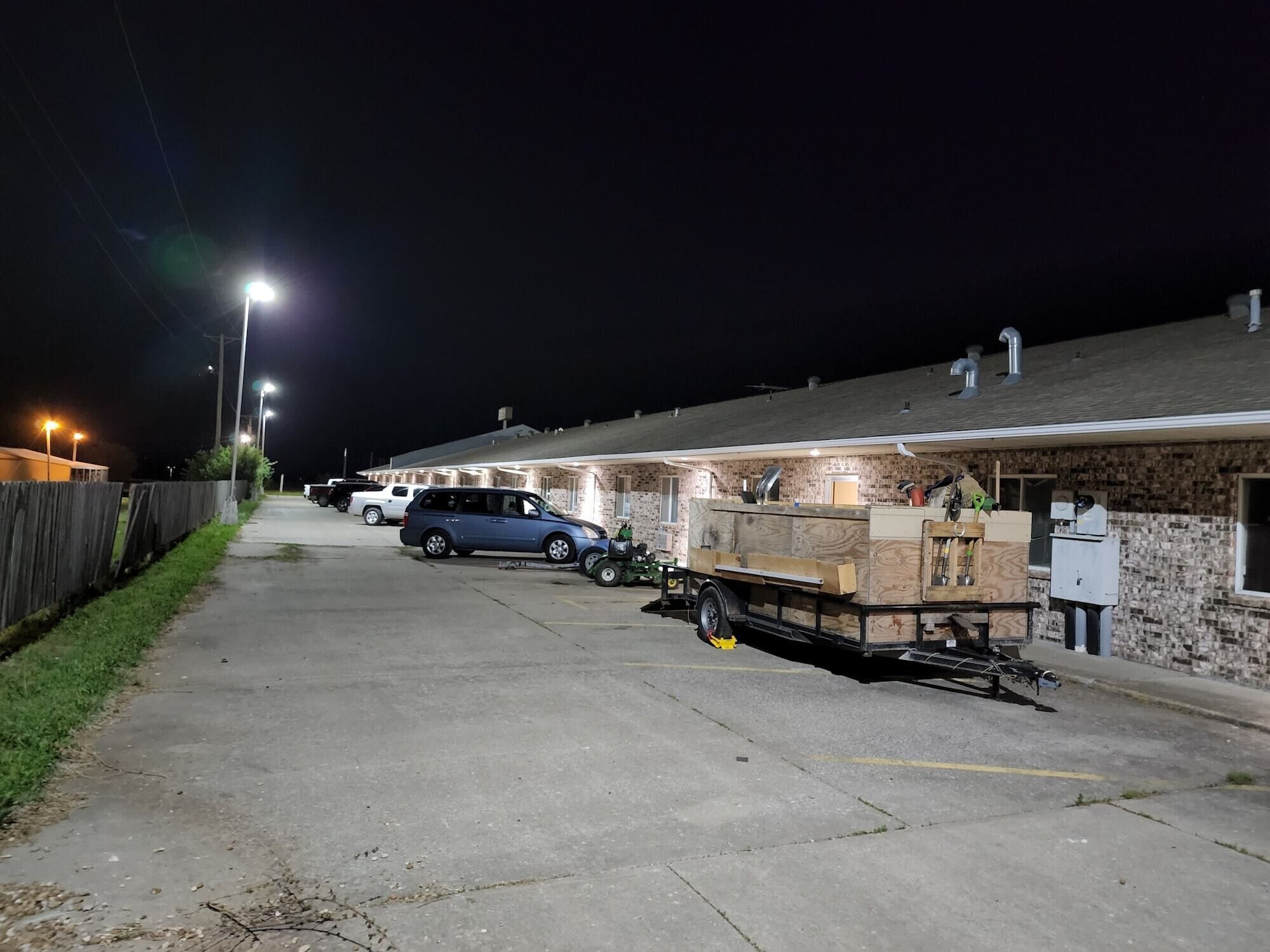 Fileira de quartos de motel com calçada pavimentada, cerca de madeira e um carro estacionado.