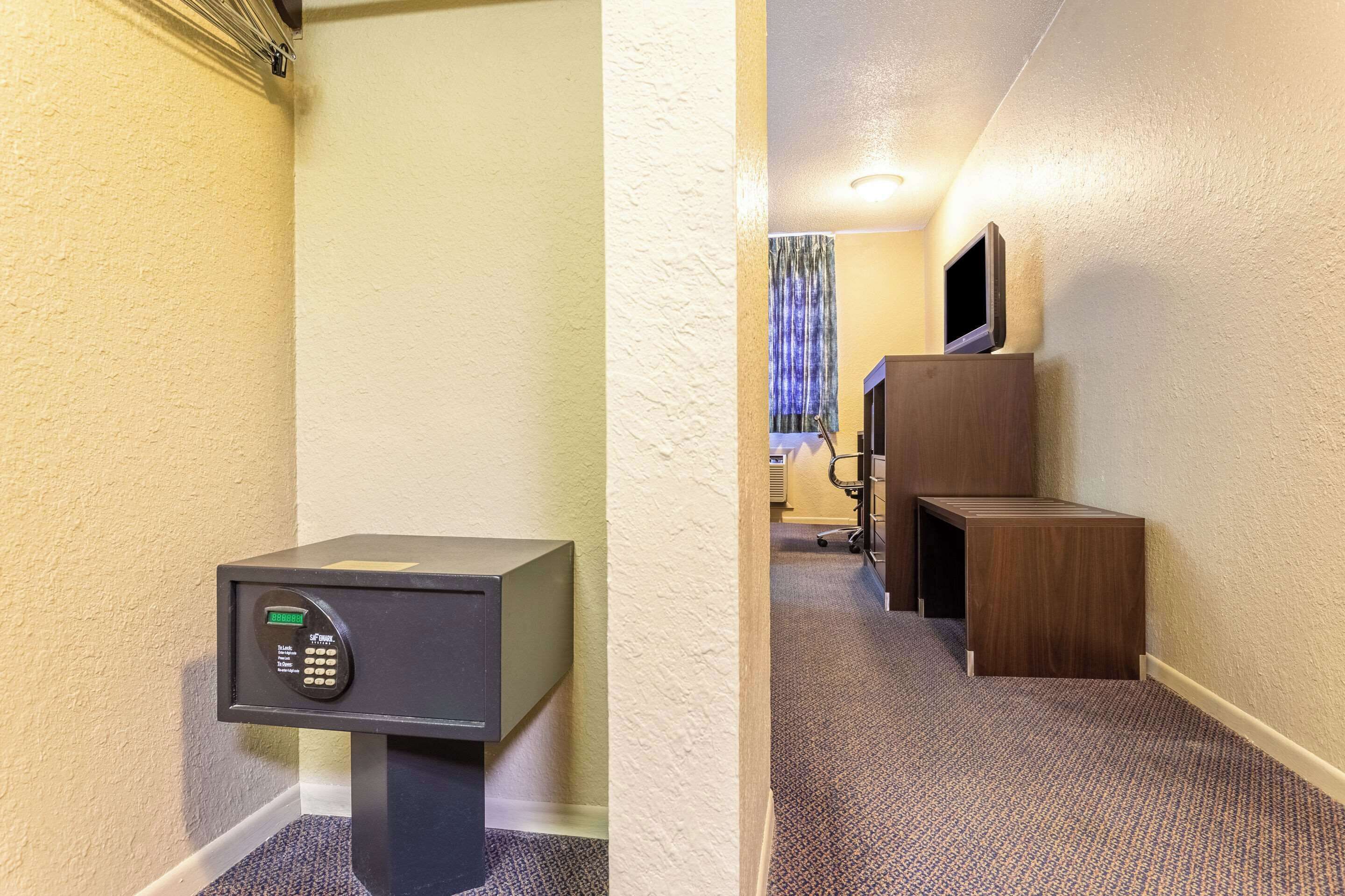 Habitación de hotel con minibar, una mesita de madera, televisor montado en la pared y piso alfombrado.