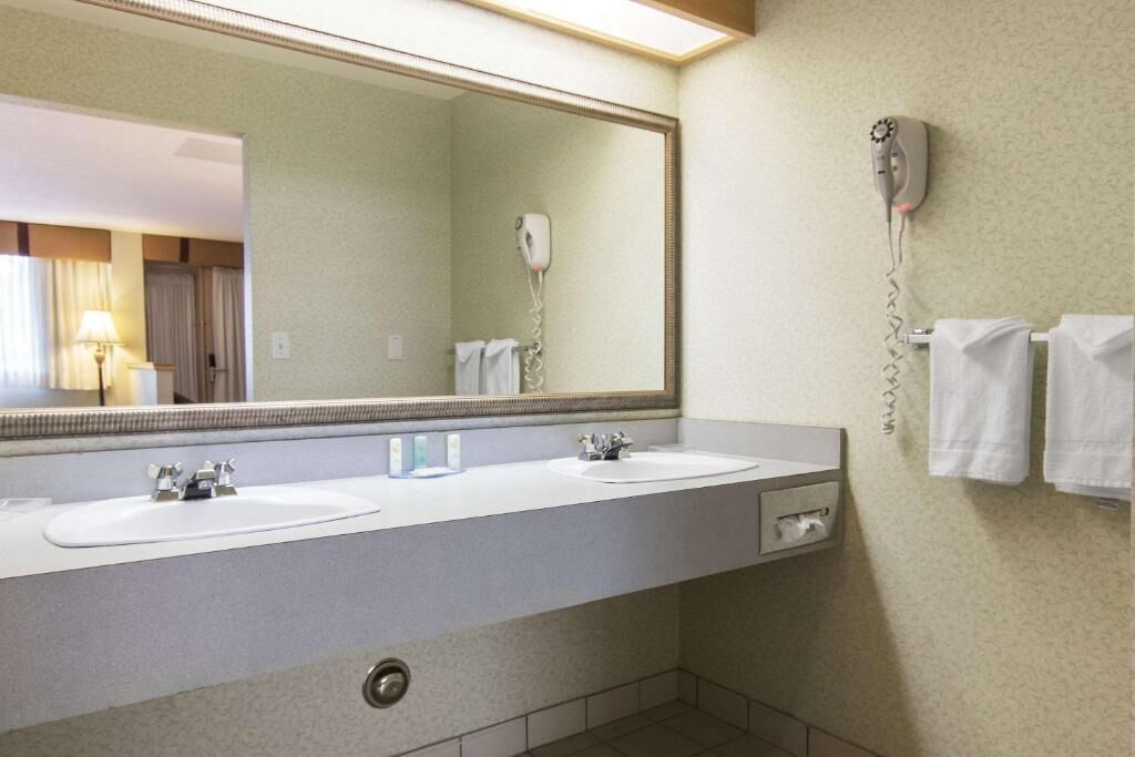 A hotel bathroom with two sinks, a large mirror, a hairdryer, and towels on the wall.