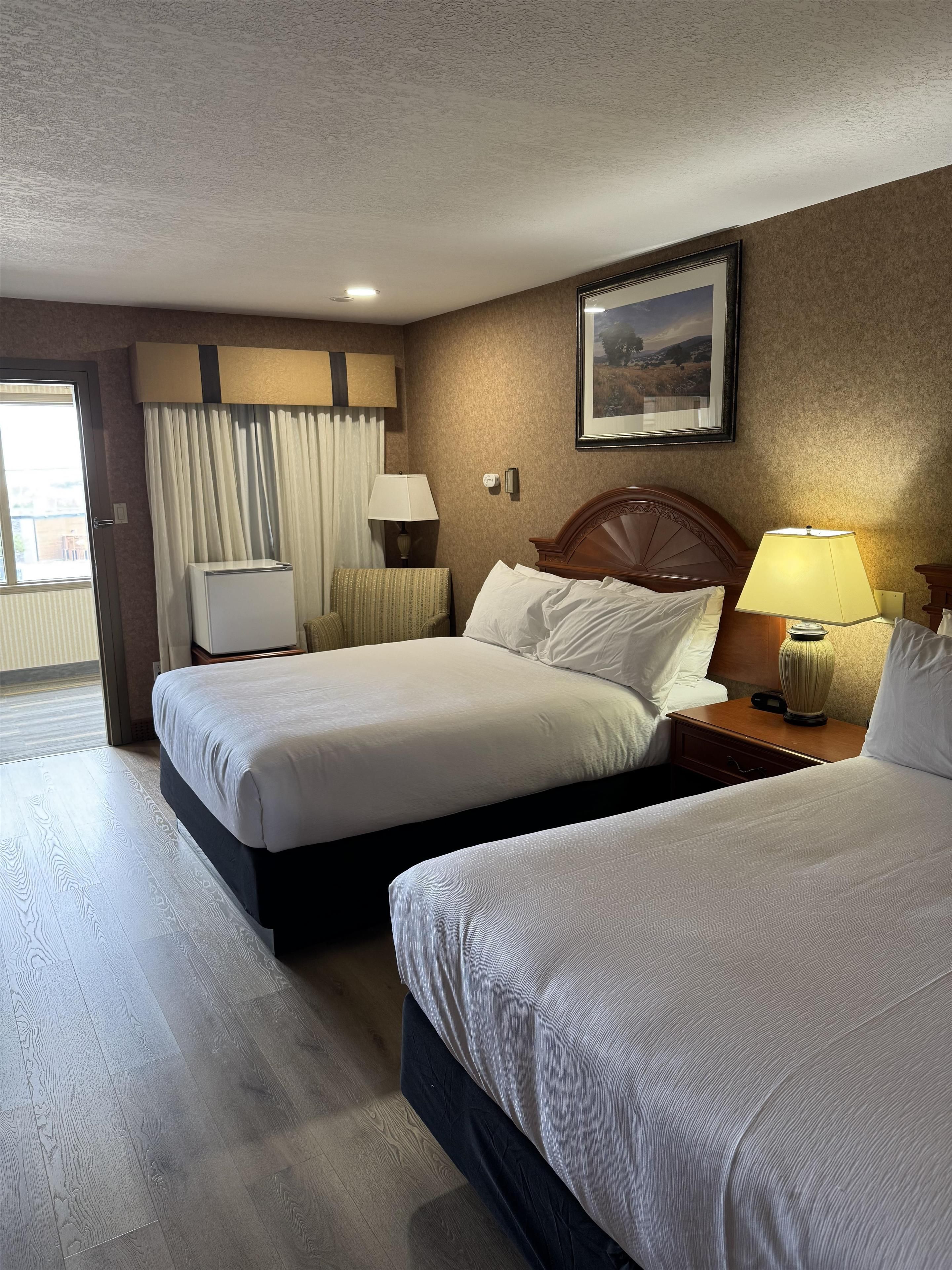 A hotel room with two beds, a television, a lamp, and a painting on the wall.