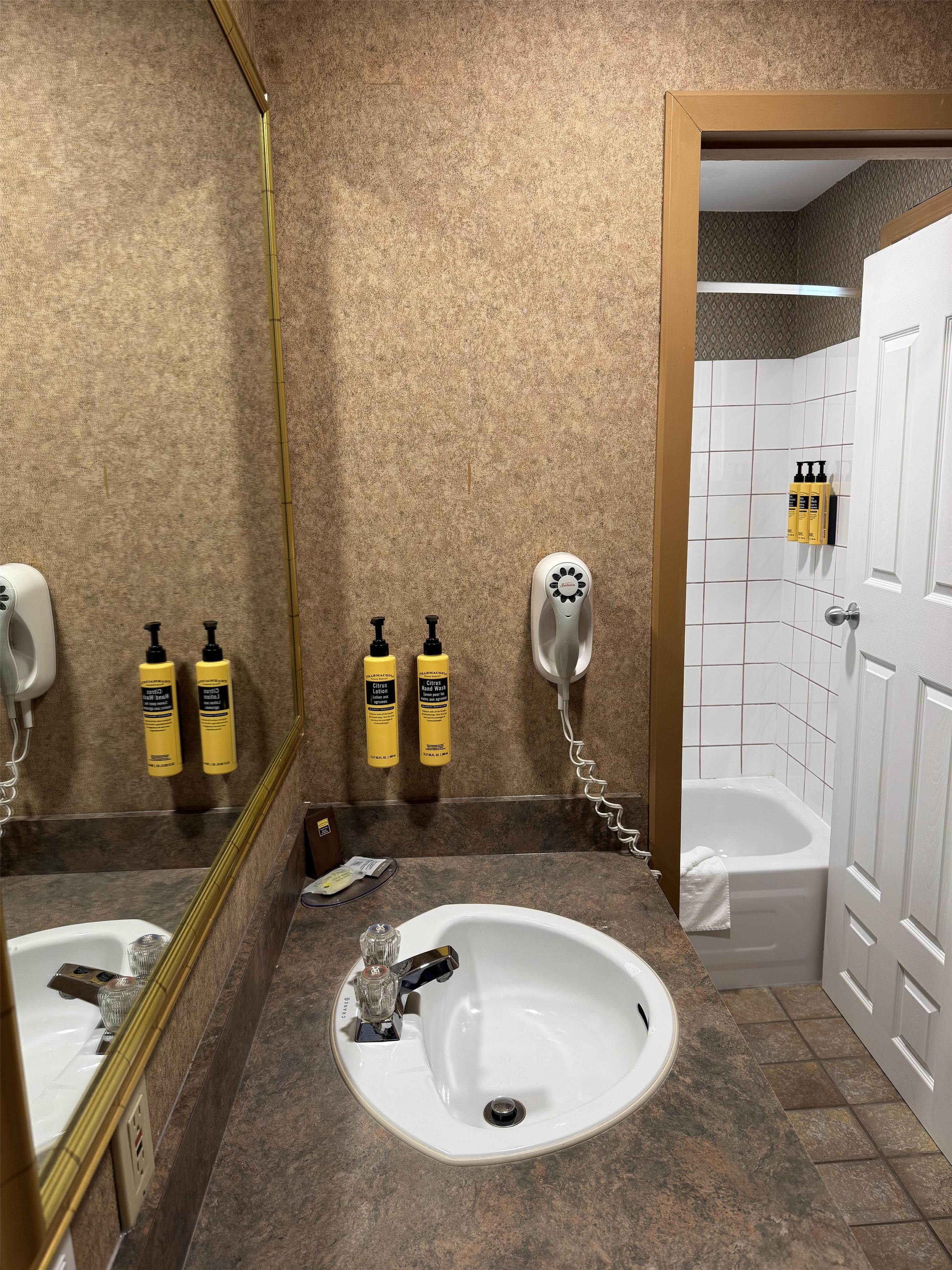 Une salle de bain équipée d’un lavabo, d’un miroir, d’un sèche-mains et d’articles de toilette.