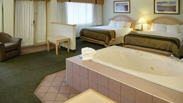 A hotel room with a large bathtub, two beds, a desk, and a chair. - Flamingo Hotel (Medicine Hat)