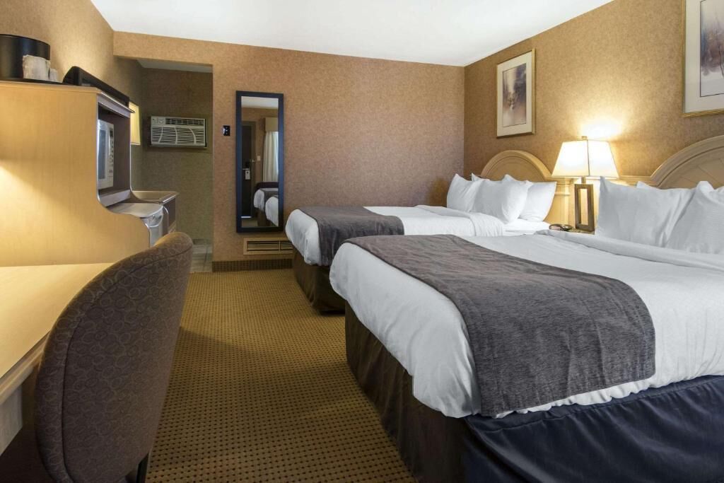 Ein Hotelzimmer mit zwei Betten, einem Schreibtisch, einem Stuhl, einem Spiegel und einer Lampe.