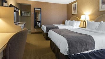 Ein Hotelzimmer mit zwei Betten, einem Schreibtisch, einem Stuhl, einem Spiegel und einer Lampe.