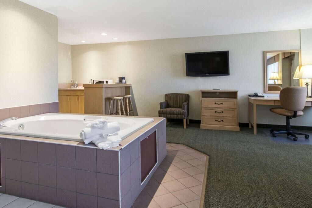Habitación de hotel con una bañera grande, un escritorio, una silla, un televisor y un espejo.