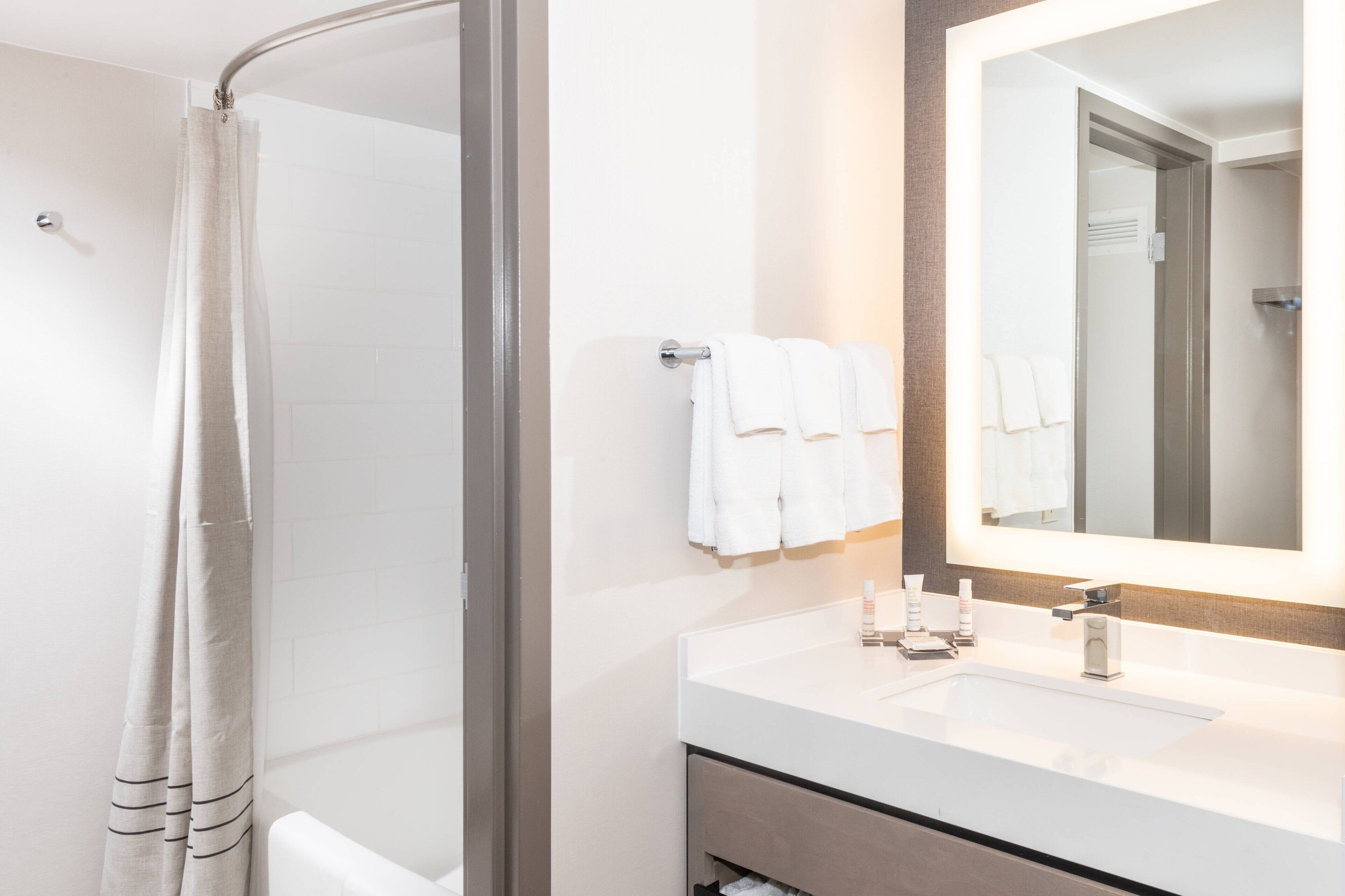 A modern bathroom with a shower, a sink with a mirror, and two towels hanging on the wall.