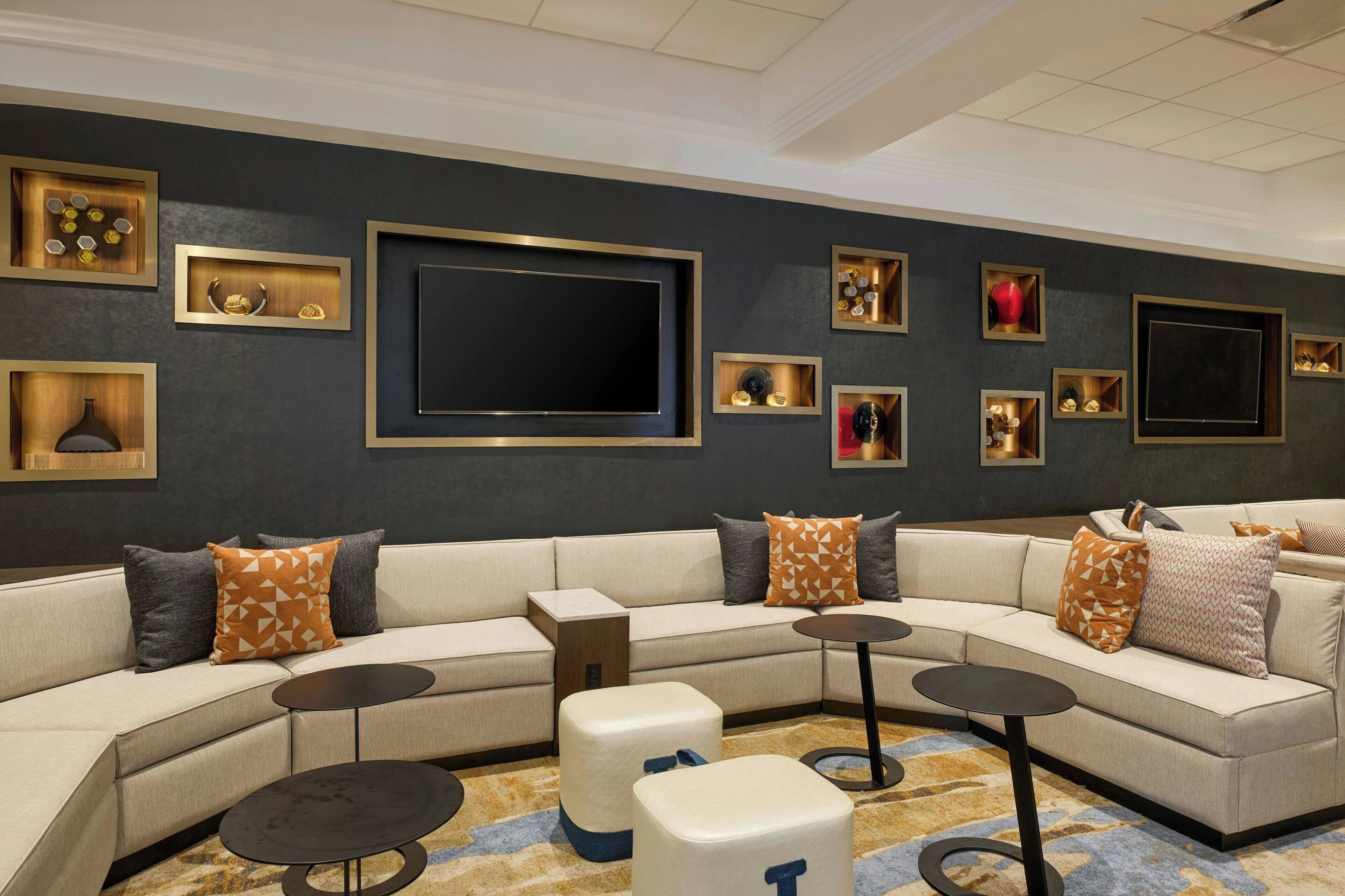 A modern living room with a sectional sofa, multiple small tables, and decorative wall shelves.
