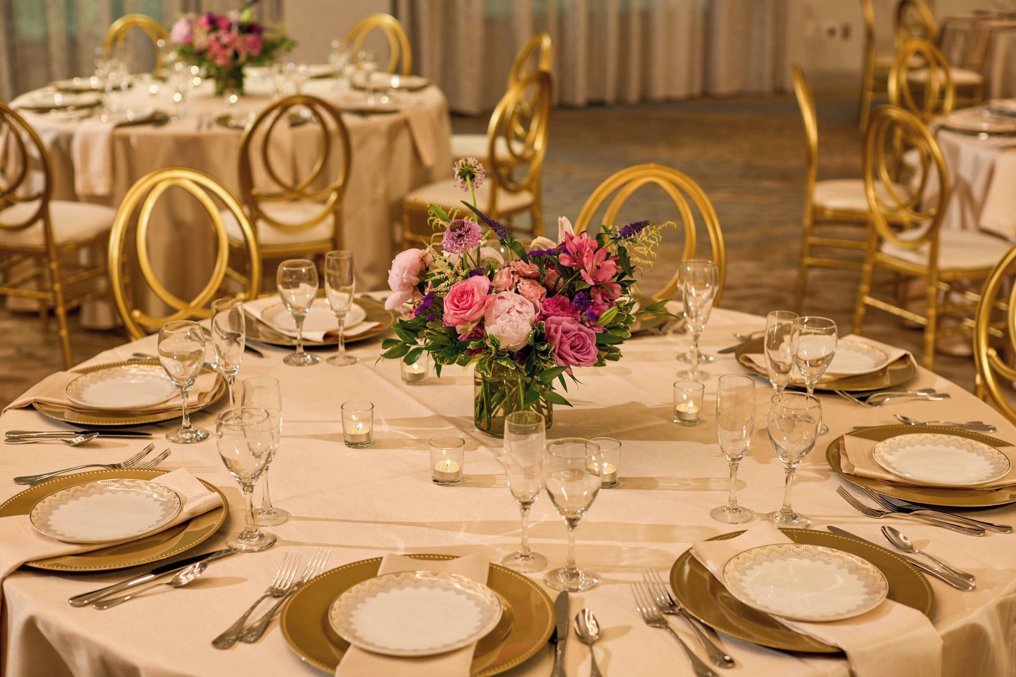 A banquet hall with round tables set for a formal event, featuring gold chairs and white tablecloths.