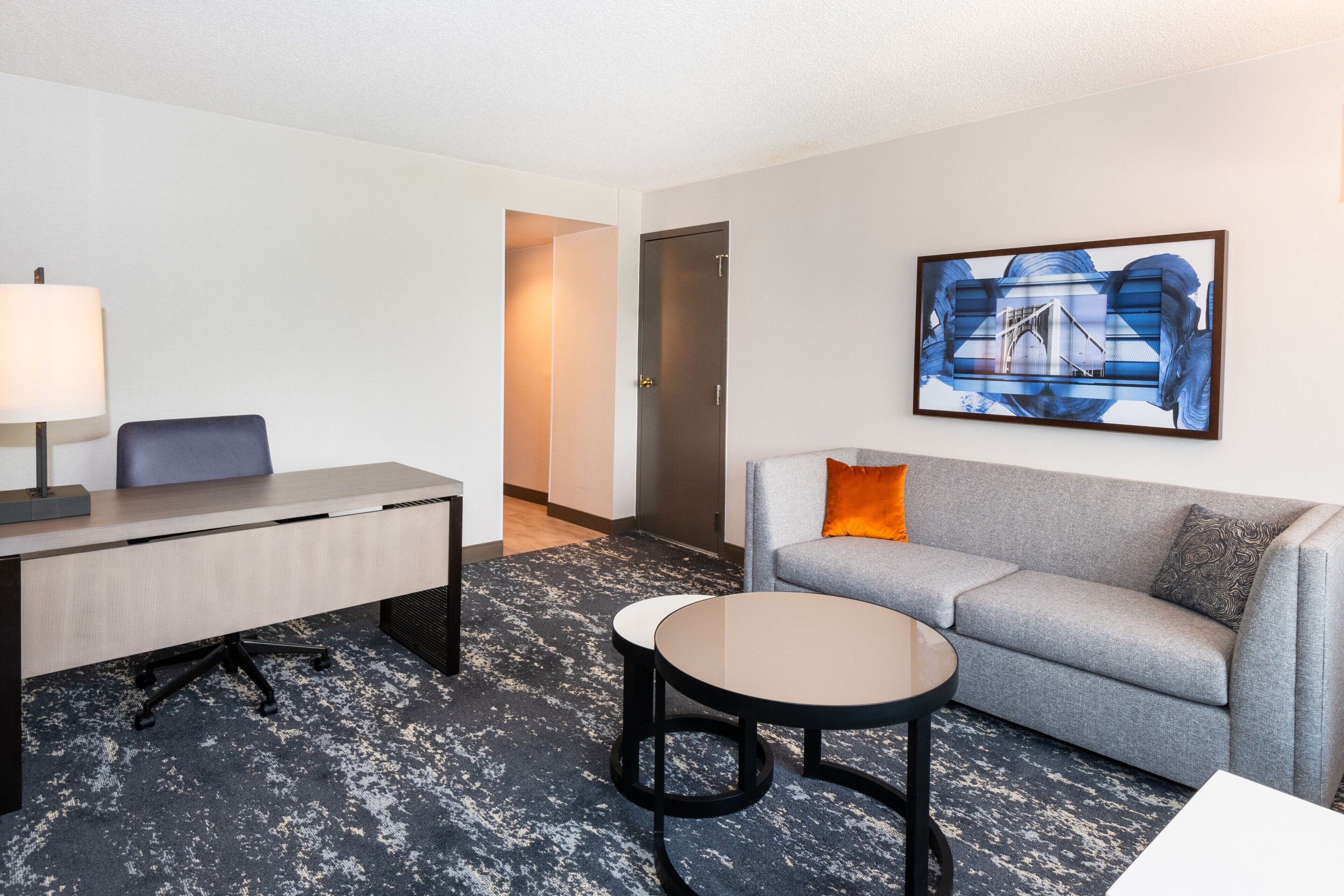 A hotel room with a desk, chair, sofa, and a round coffee table.